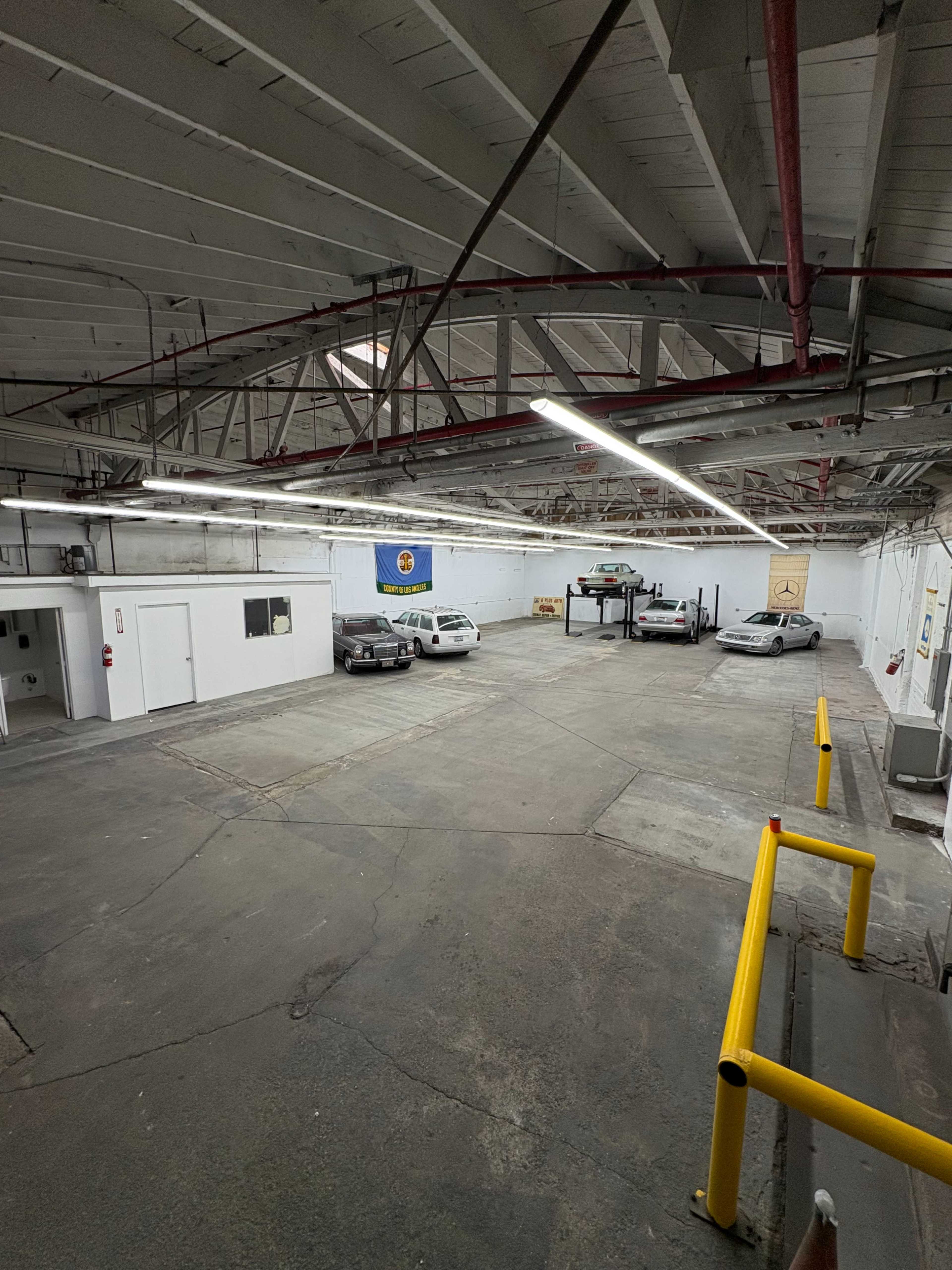 The image shows a spacious, empty garage area with several parked cars and industrial lighting overhead.