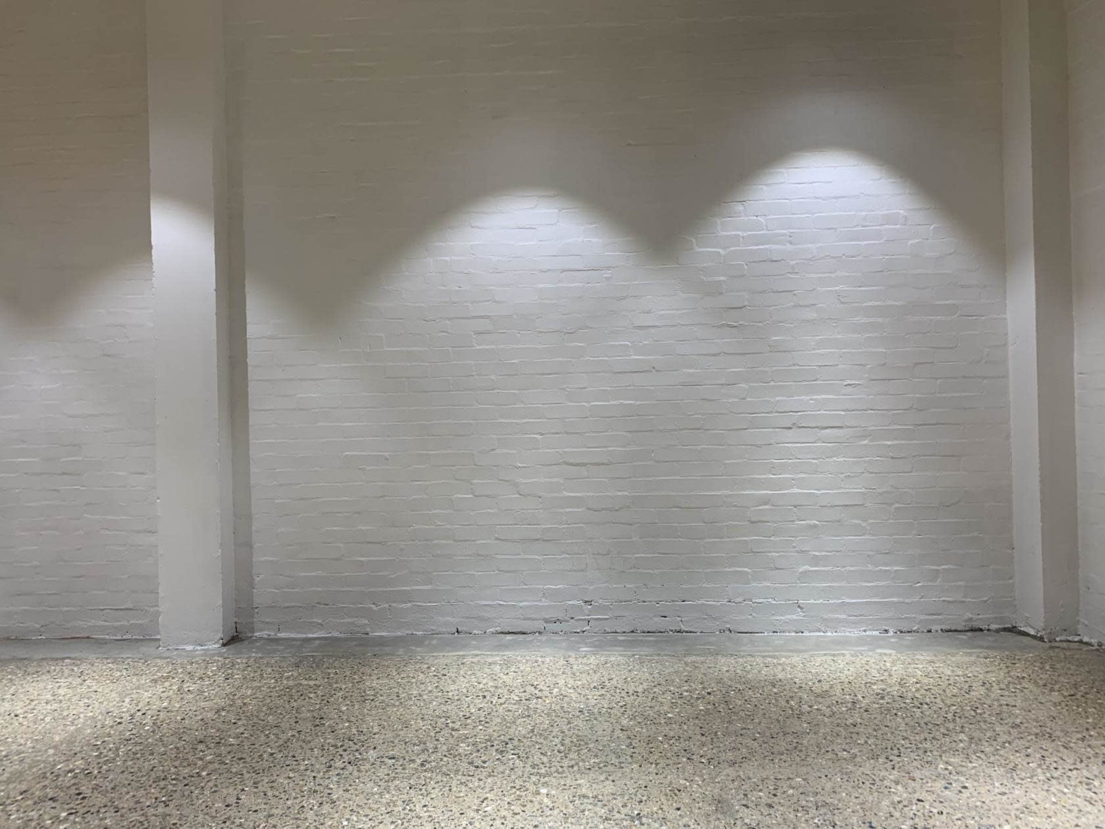 A clean, white brick wall with three evenly spaced light spots above a textured concrete floor.