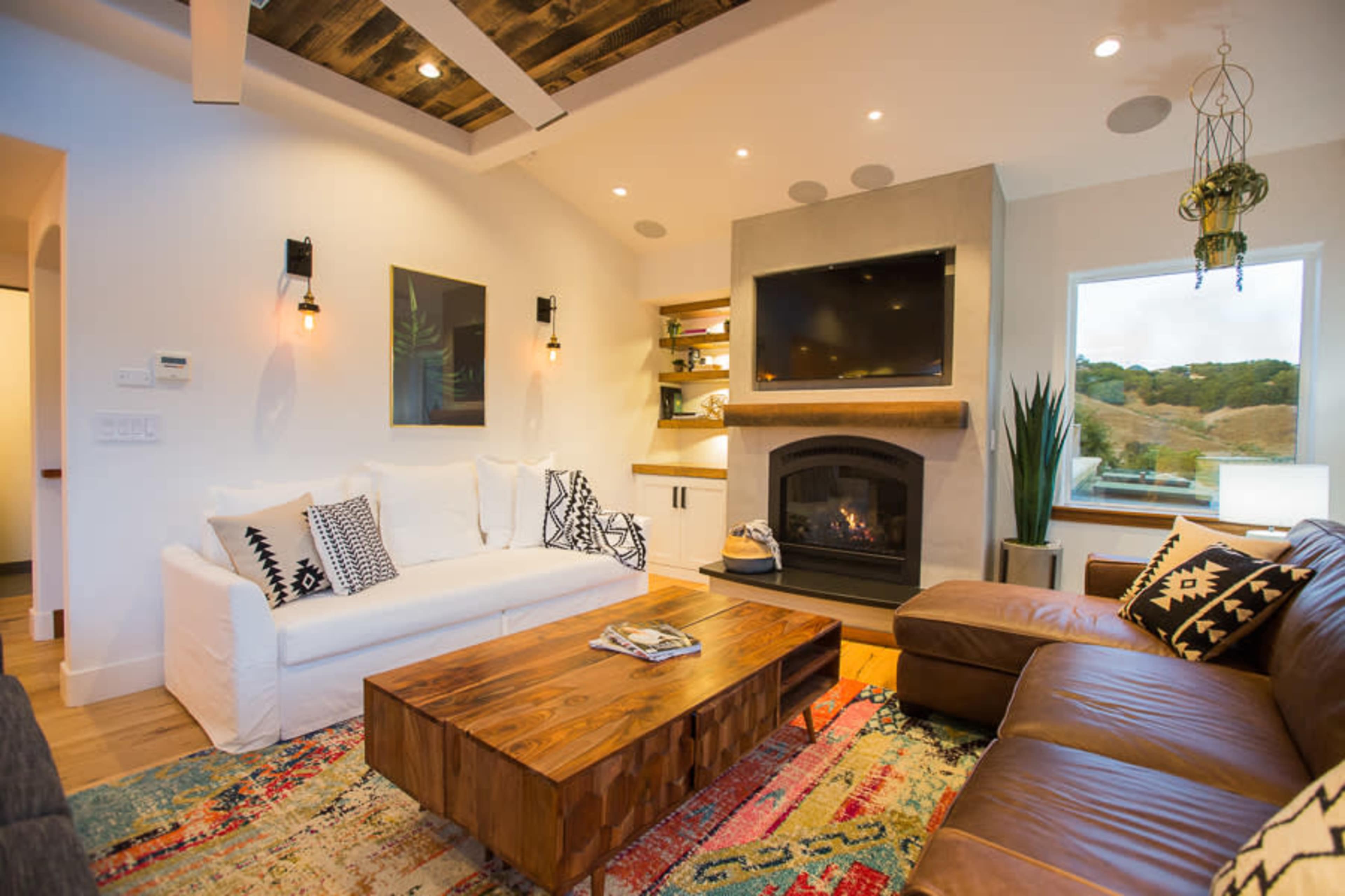 A modern living room featuring a white sofa, a brown leather sectional, a wooden coffee table, and a fireplace beneath a wall-mounted television.