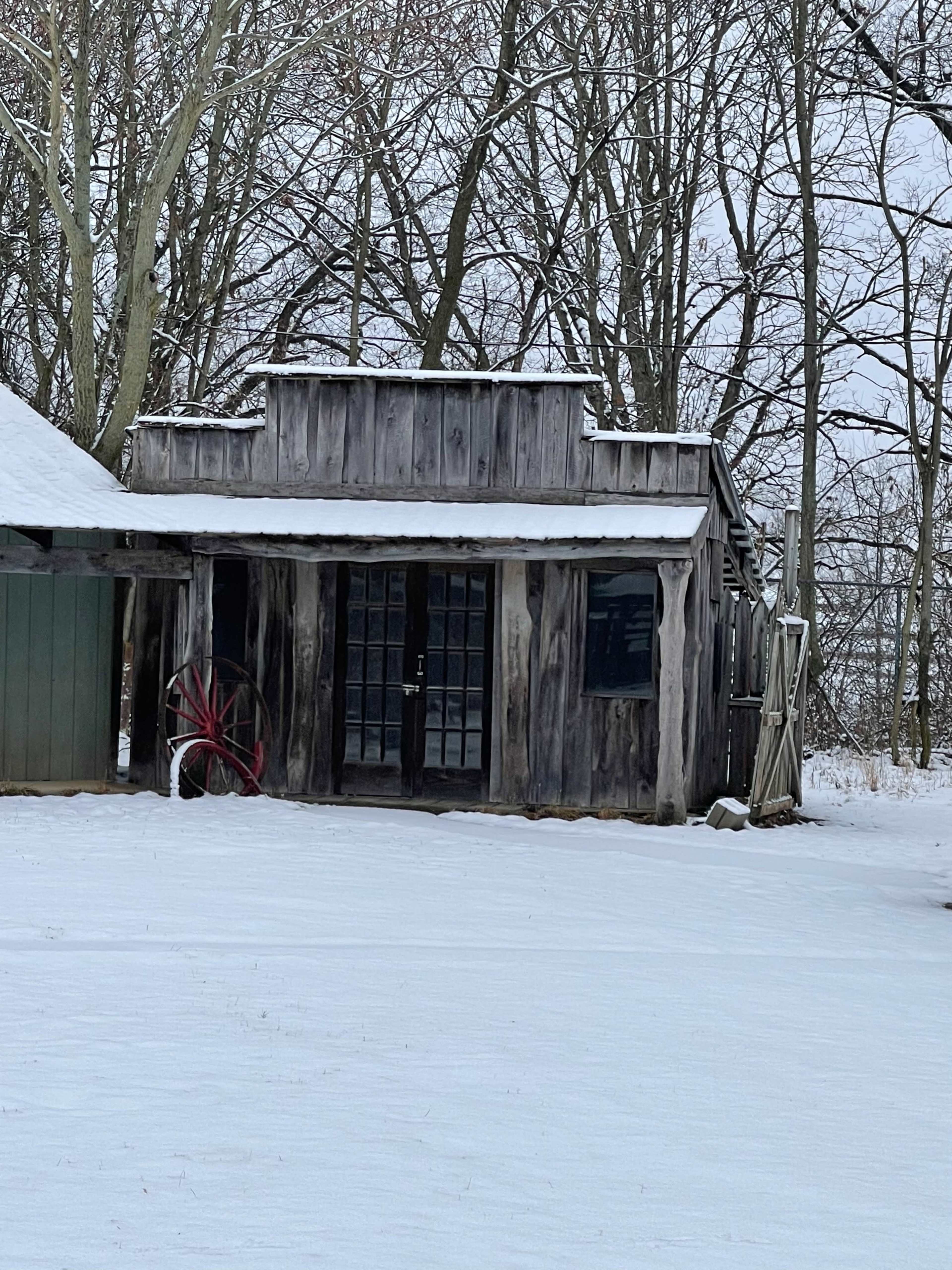 A rustic wooden building with glass doors is surrounded by a snowy landscape and bare trees.
