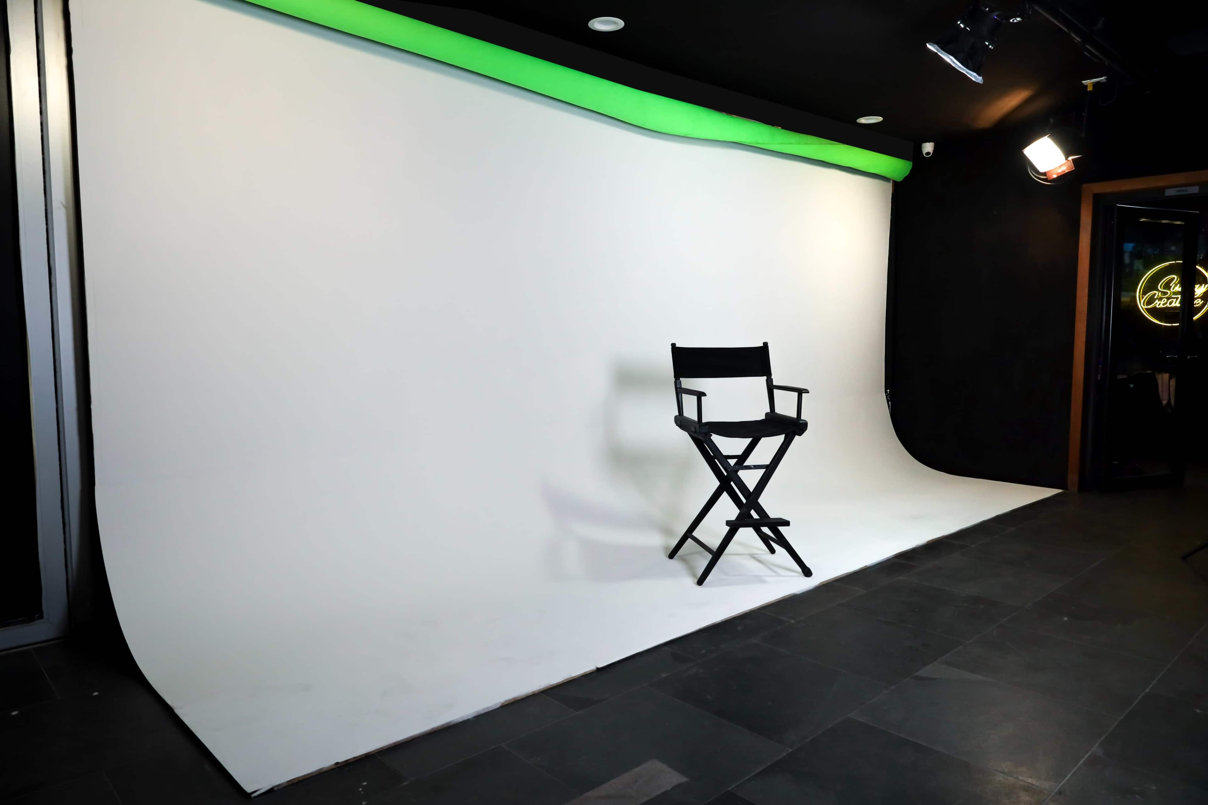 A minimalist photo studio with a white backdrop and a director's chair positioned on a dark tiled floor.