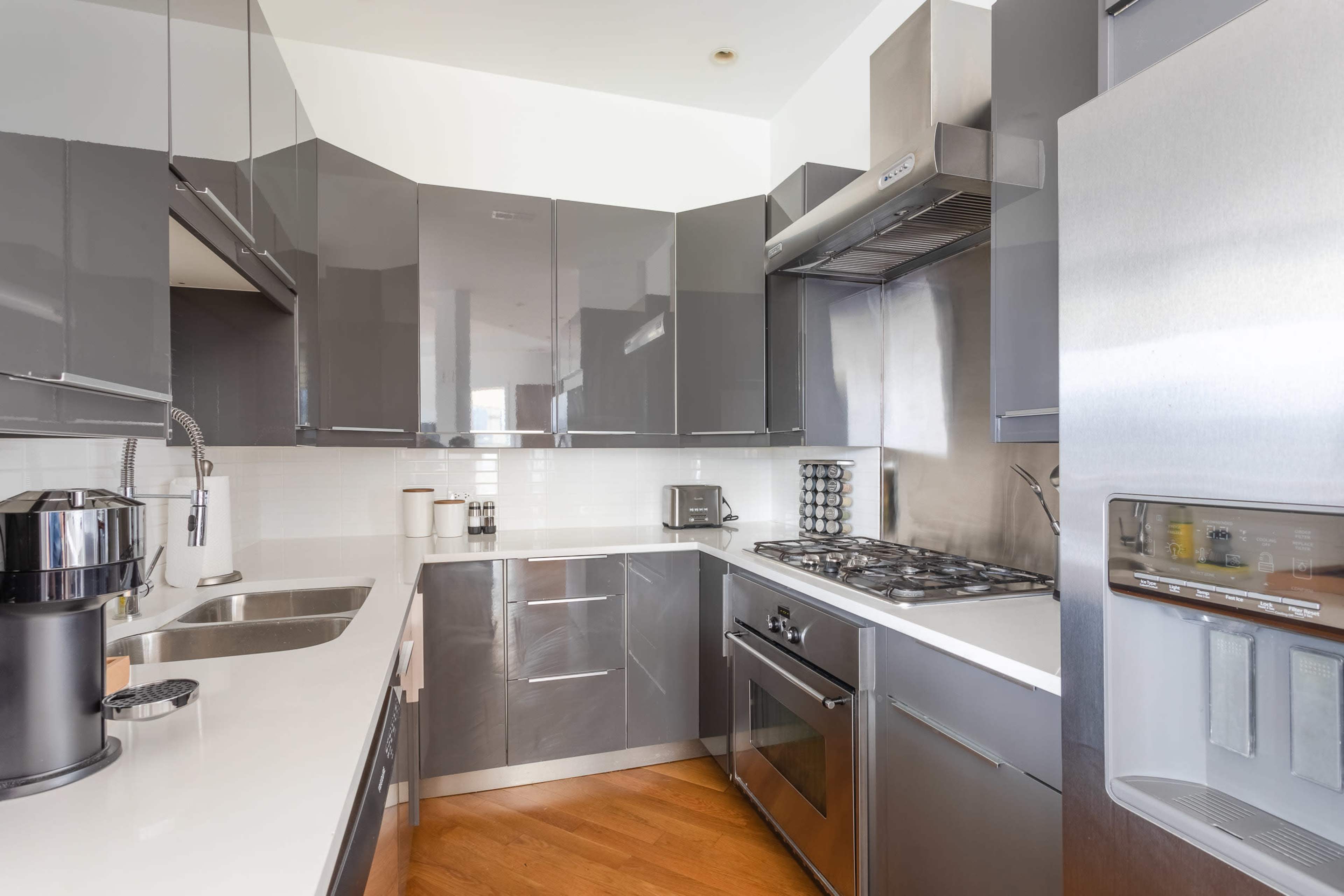 A modern kitchen features sleek gray cabinets, stainless steel appliances, and a white countertop.