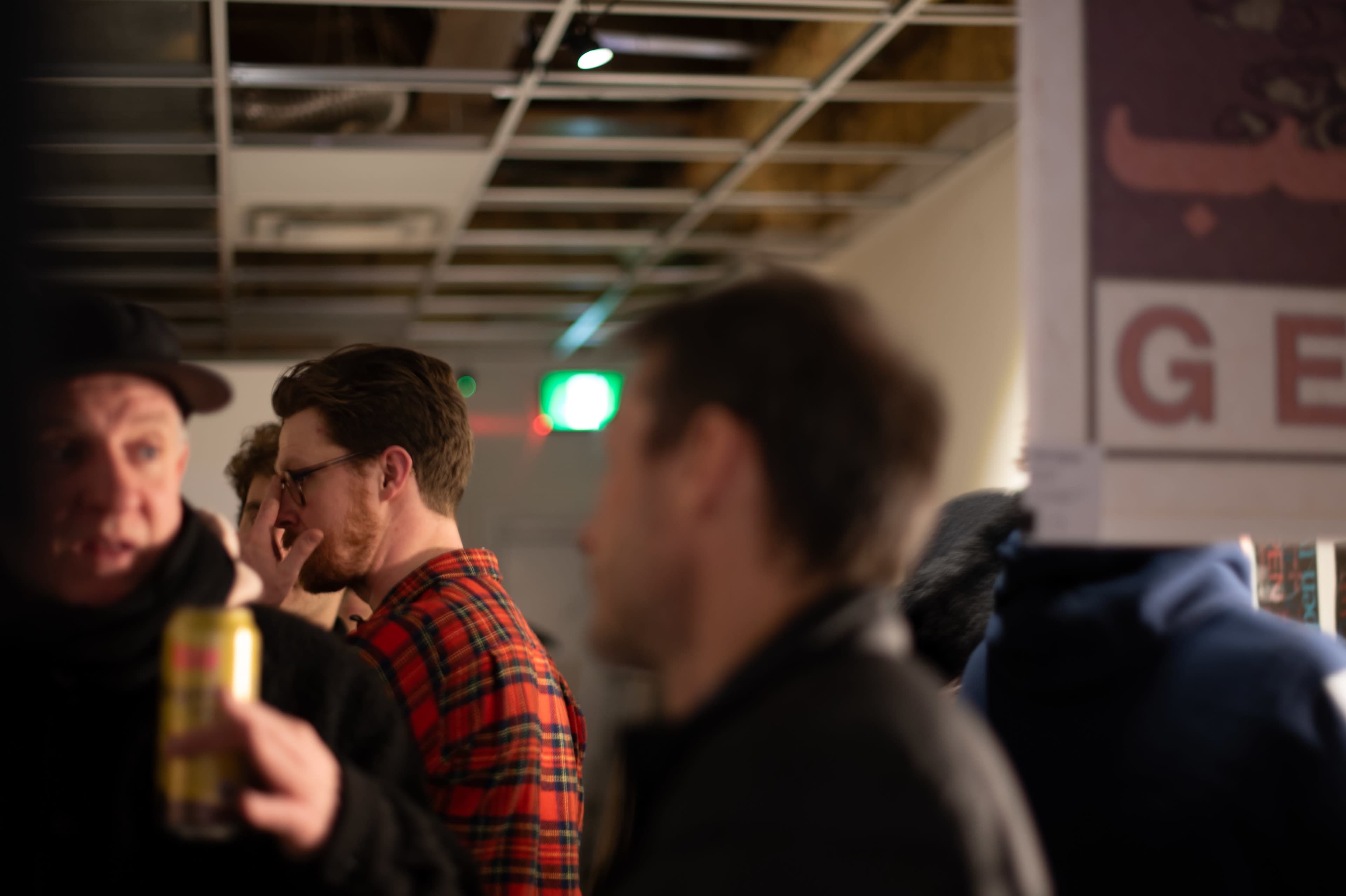 A group of people is engaged in conversation in a room with exposed ceilings and dim lighting.