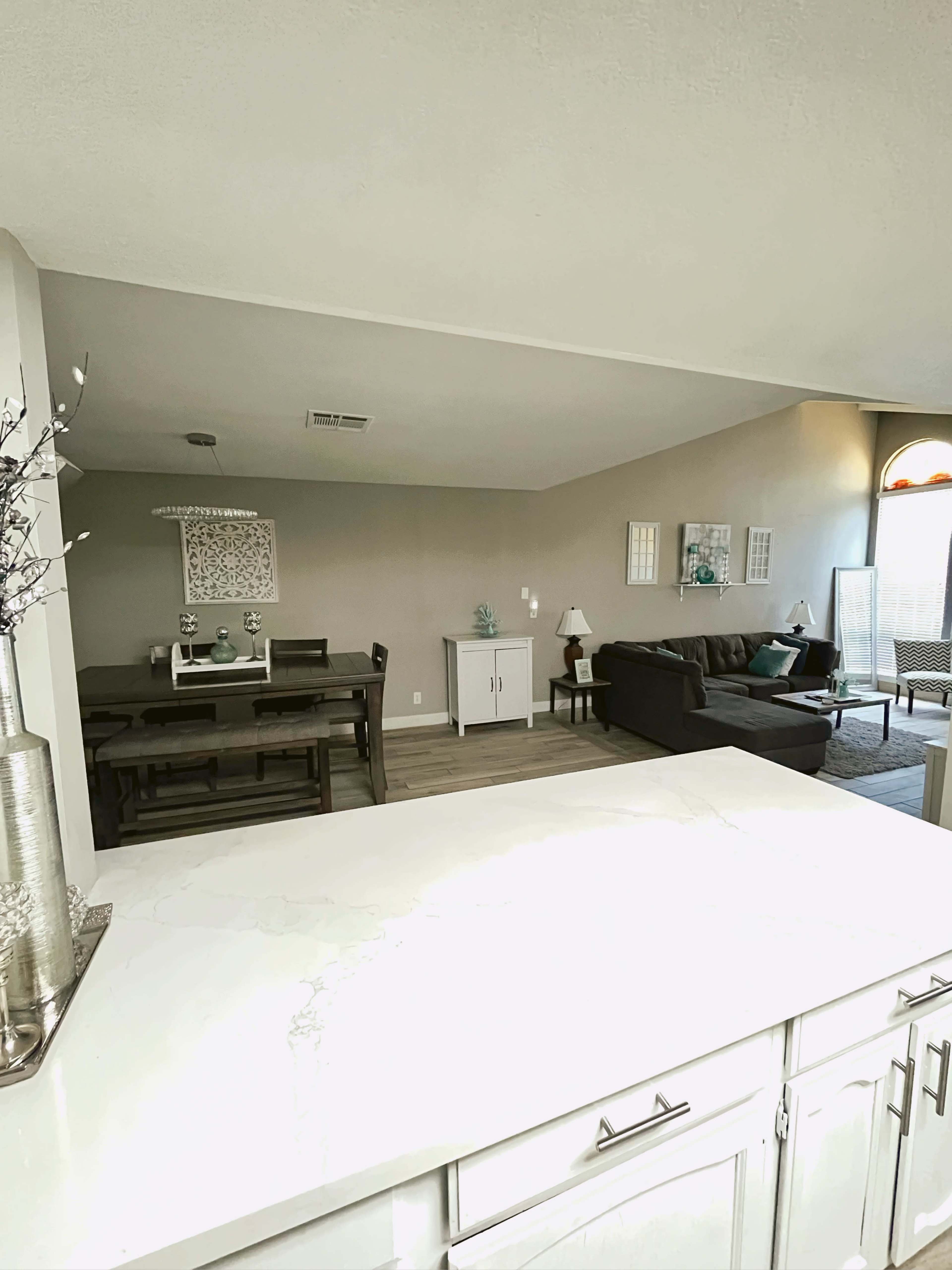 A view of an open-concept living room and dining area, featuring light-colored walls, a dining table, and a couch positioned in a spacious layout.