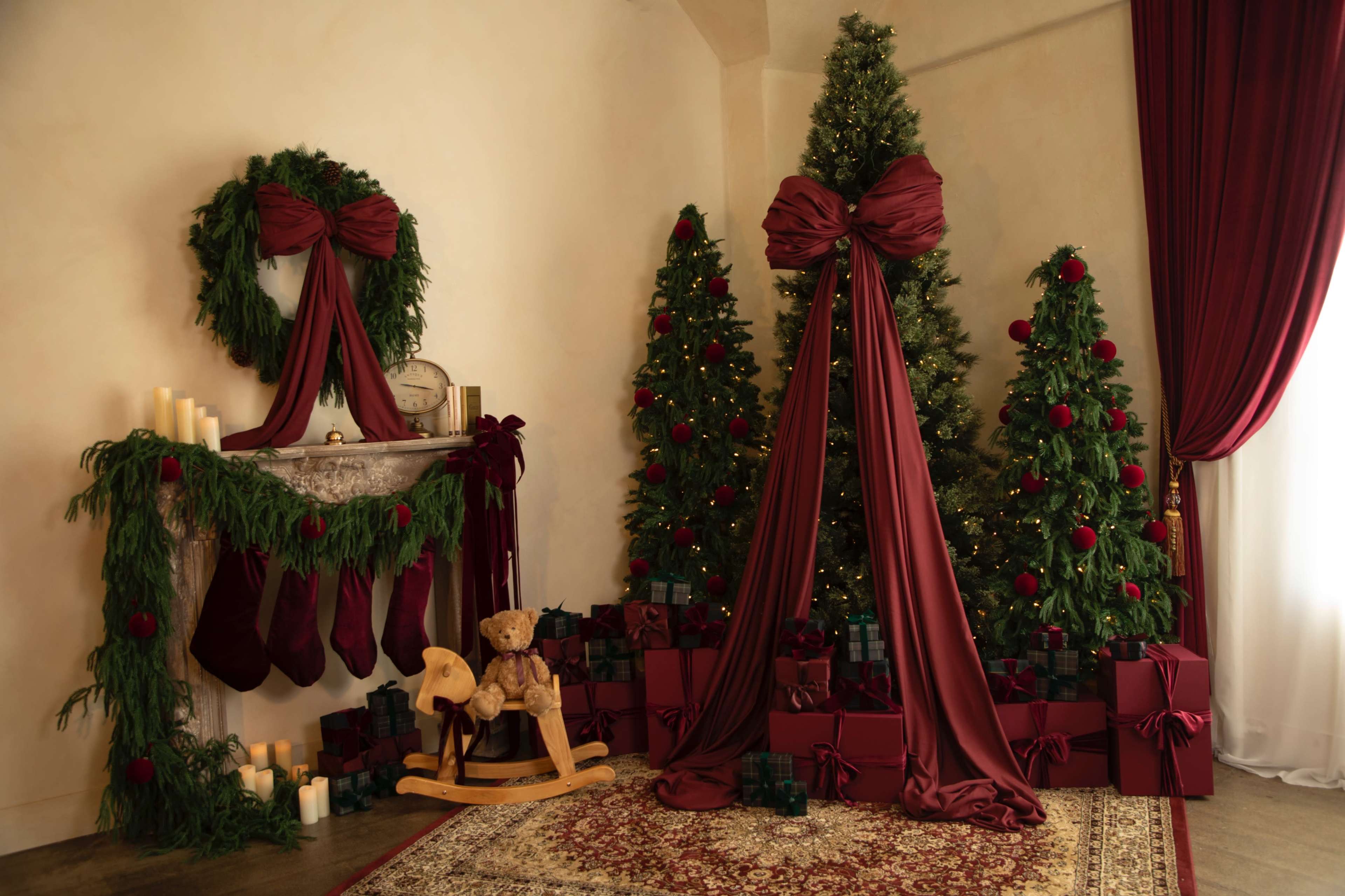 The scene features a decorated corner with two Christmas trees adorned with lights and bows, surrounded by wrapped gifts and stockings hanging on a mantle.