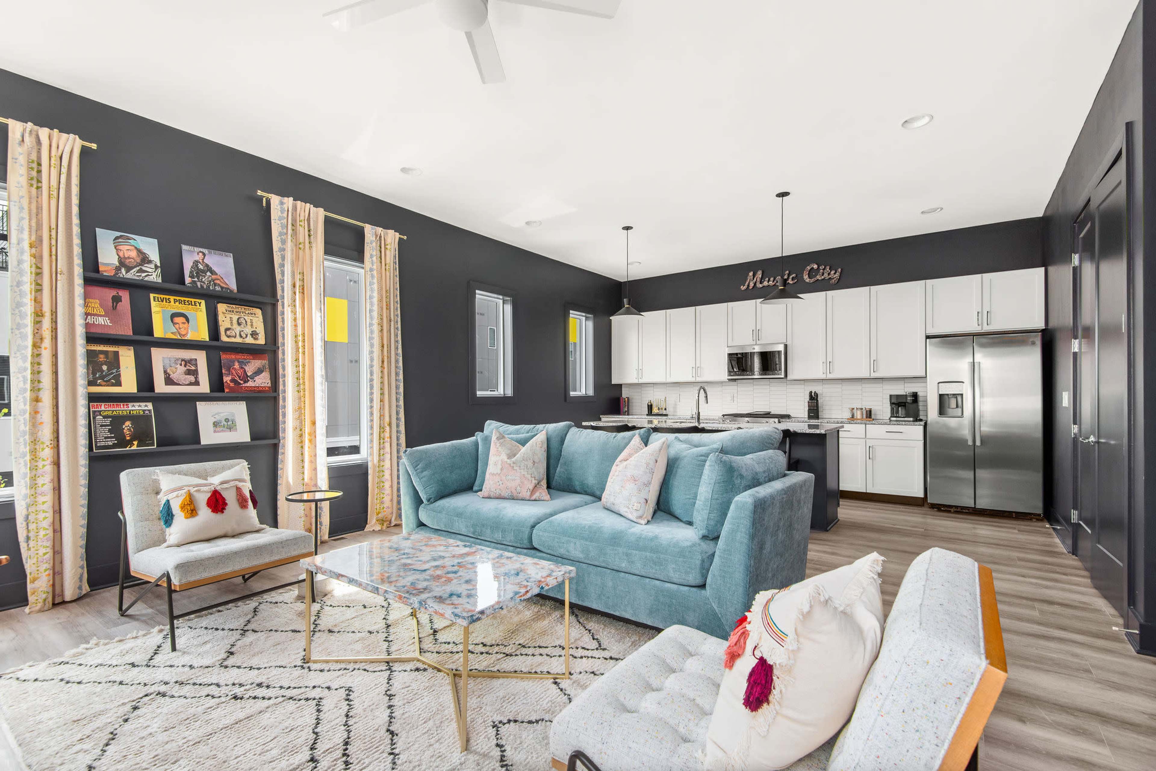 A modern living space with a light blue couch, a patterned rug, and an open kitchen featuring white cabinets and stainless steel appliances.