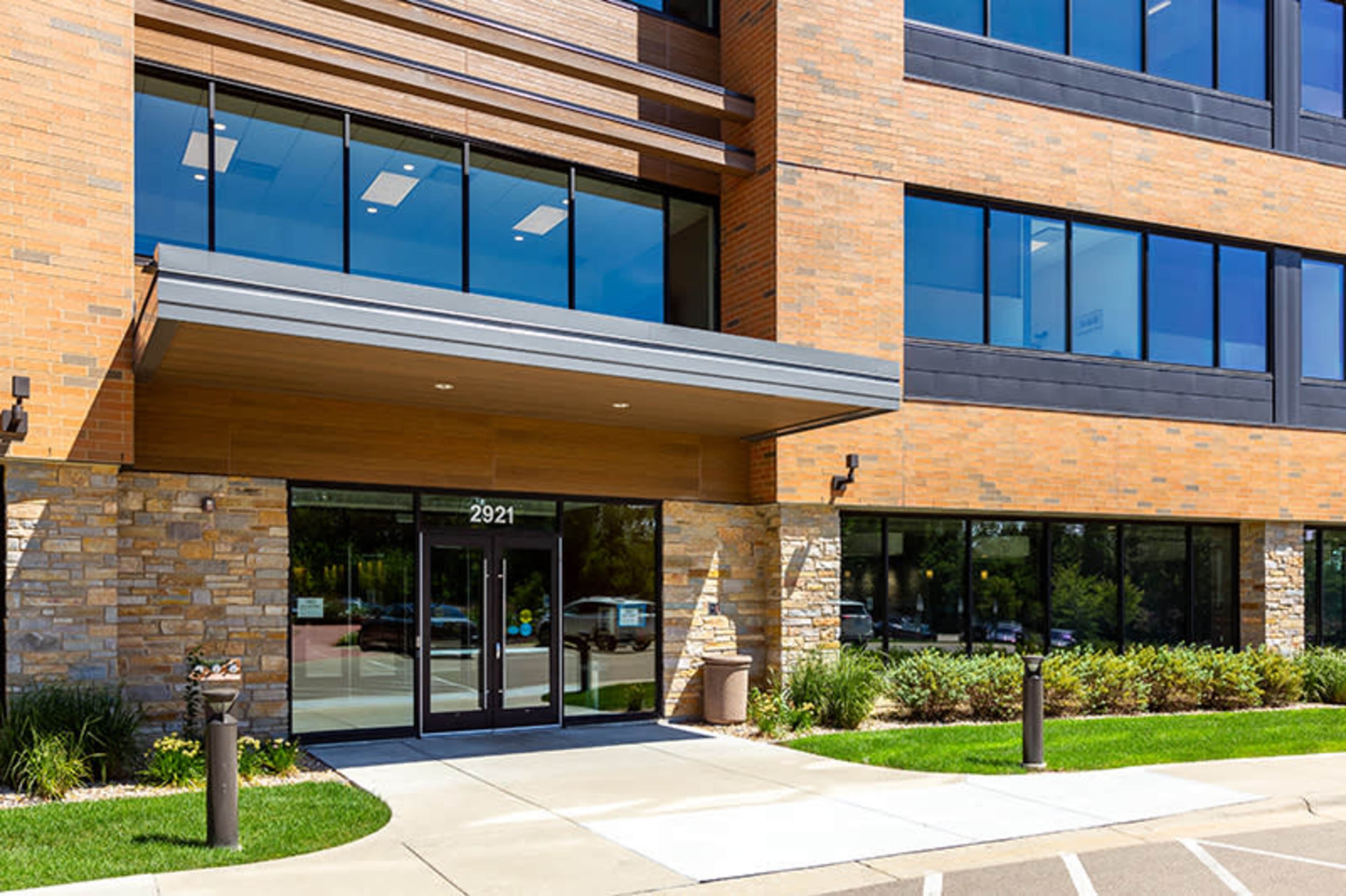 The entrance of a modern, multi-story building with large glass doors and a stone-accented facade.