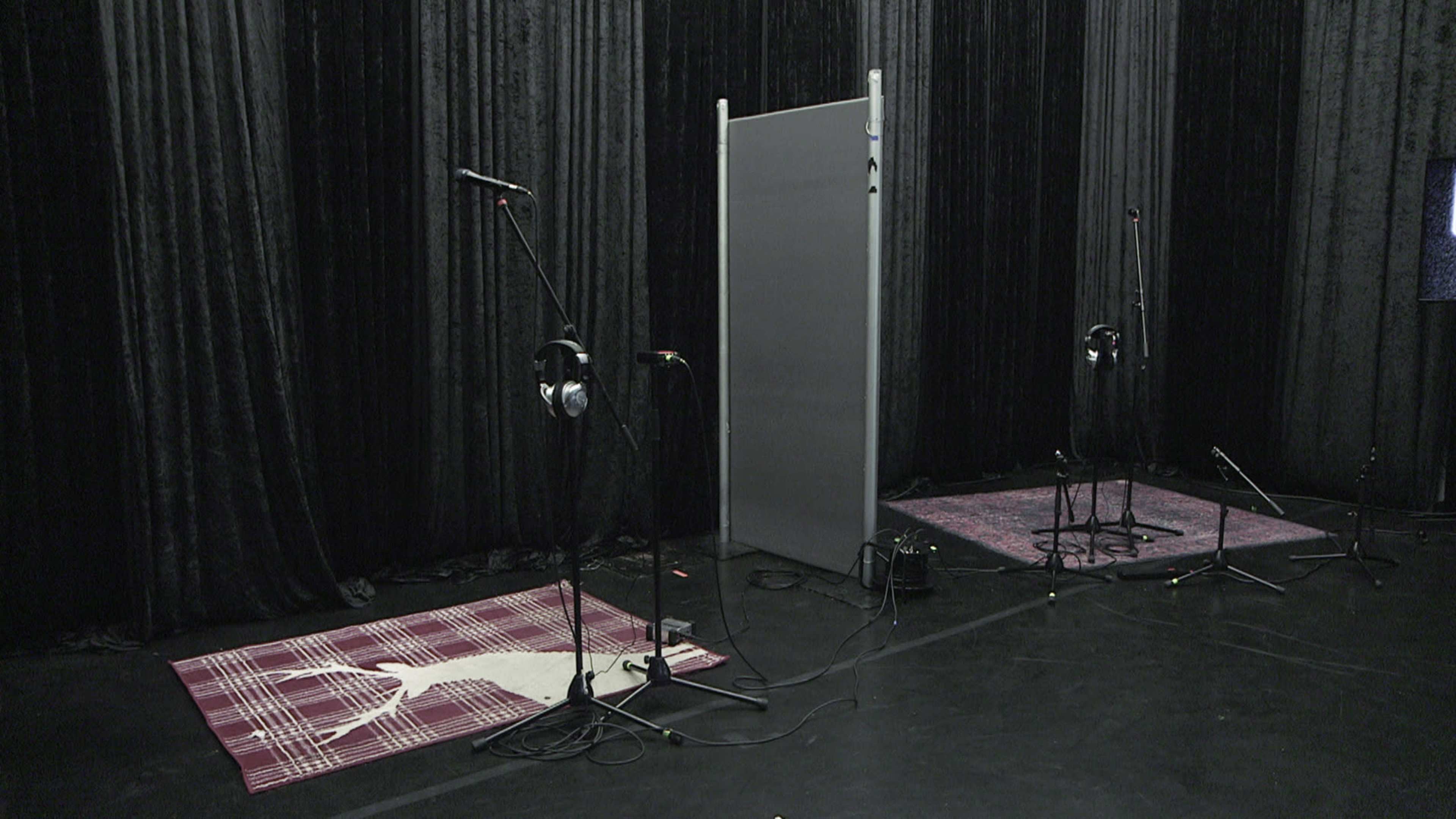 A recording studio space with microphones, headphones, and sound-absorbing panels set against a backdrop of black curtains.