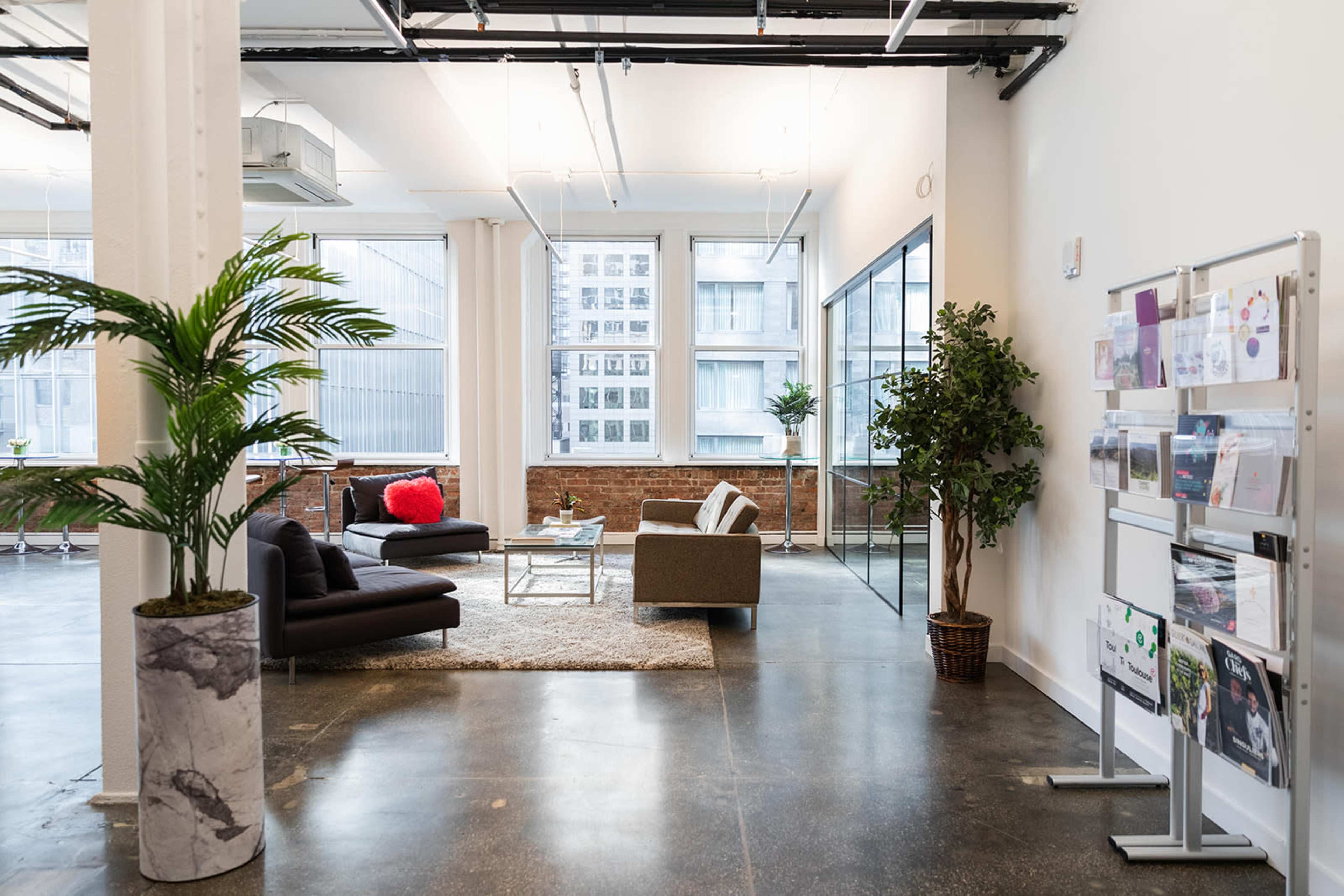 A modern office space with a seating area, large windows, and a display stand for brochures.
