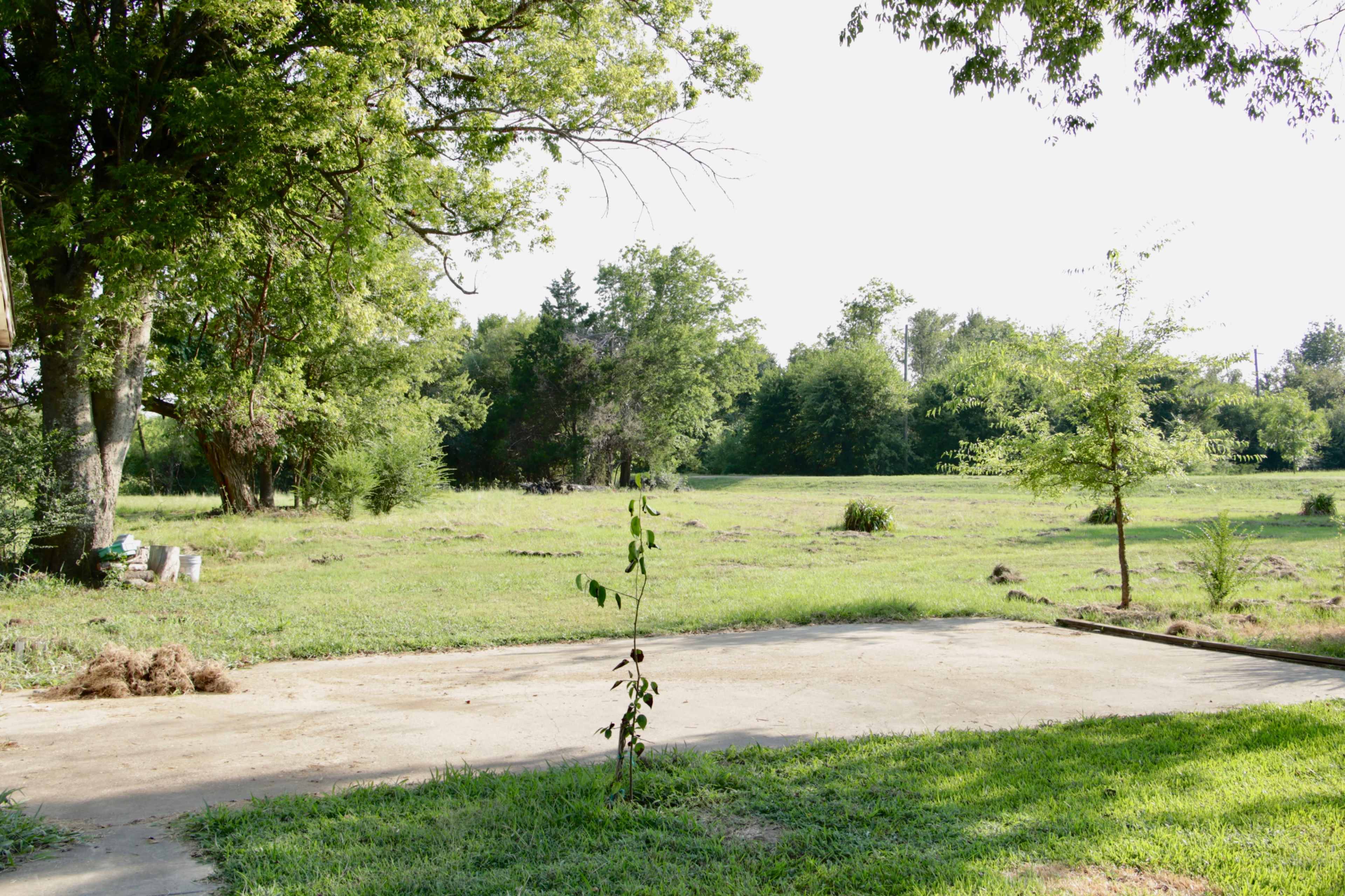The image shows a cleared concrete pad surrounded by a grassy field and trees.