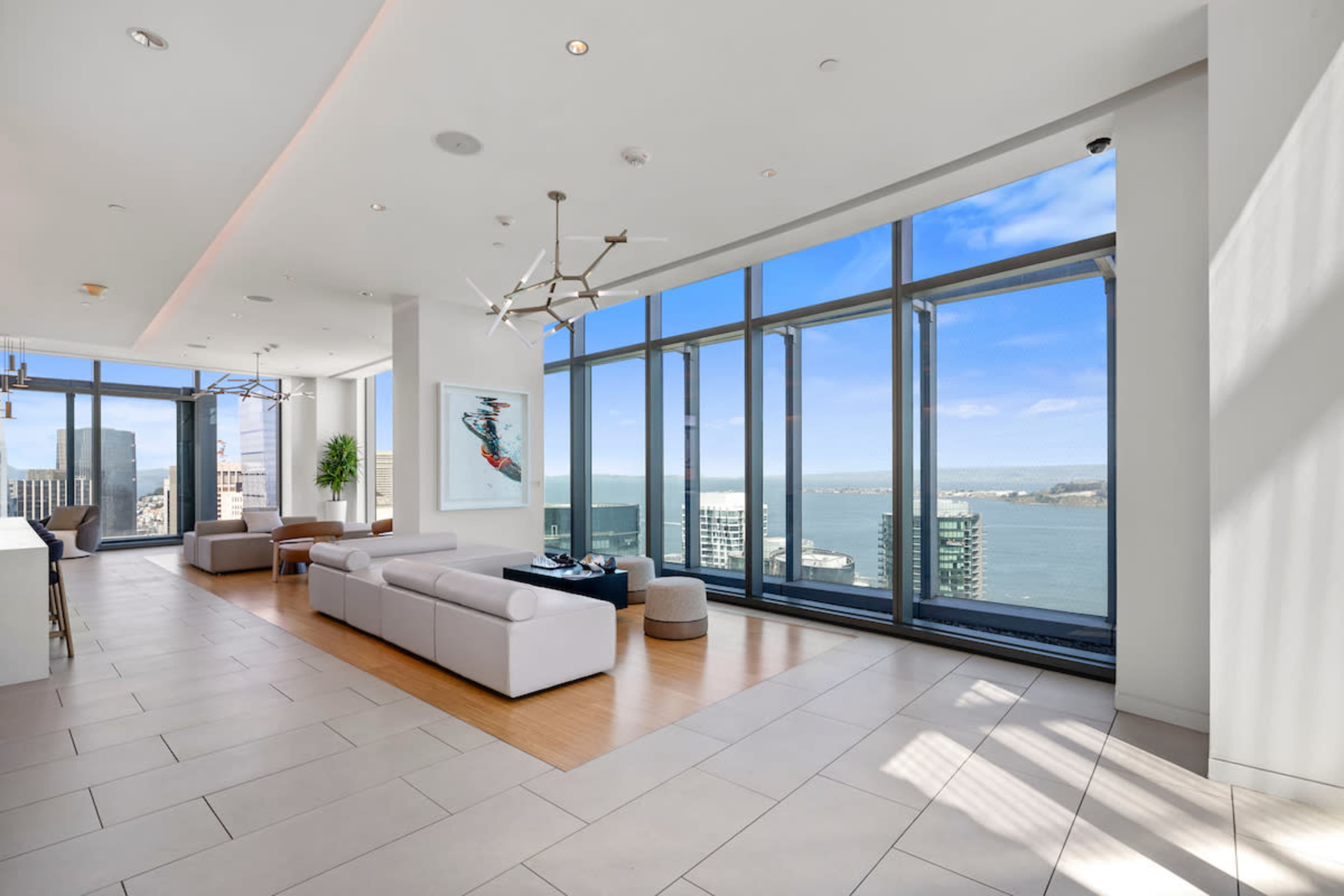 The spacious interior features large windows that offer a view of the water and city skyline, with modern furniture arranged neatly in the open living area.