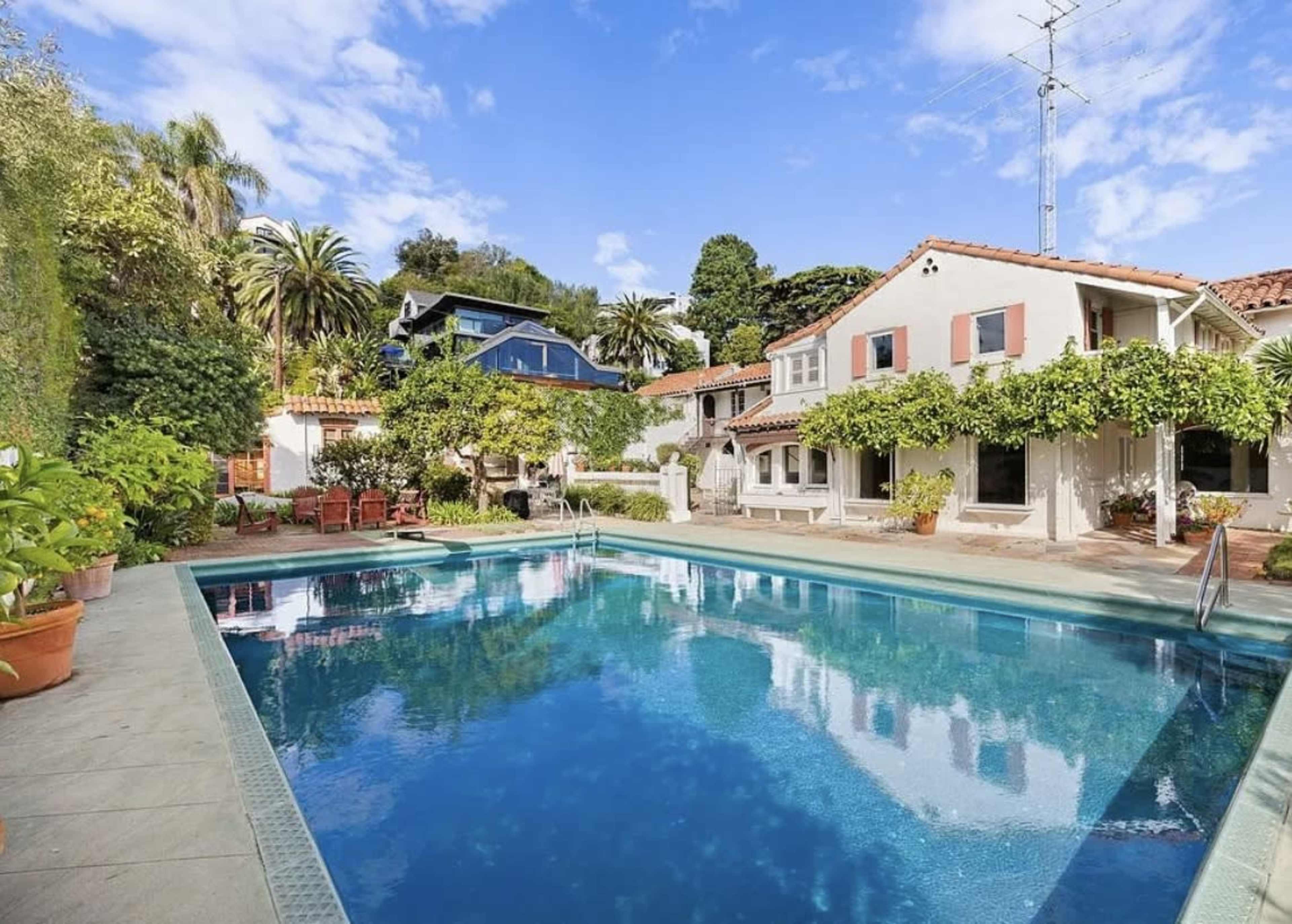 The image shows a landscaped backyard with a swimming pool surrounded by palm trees and Mediterranean-style architecture.