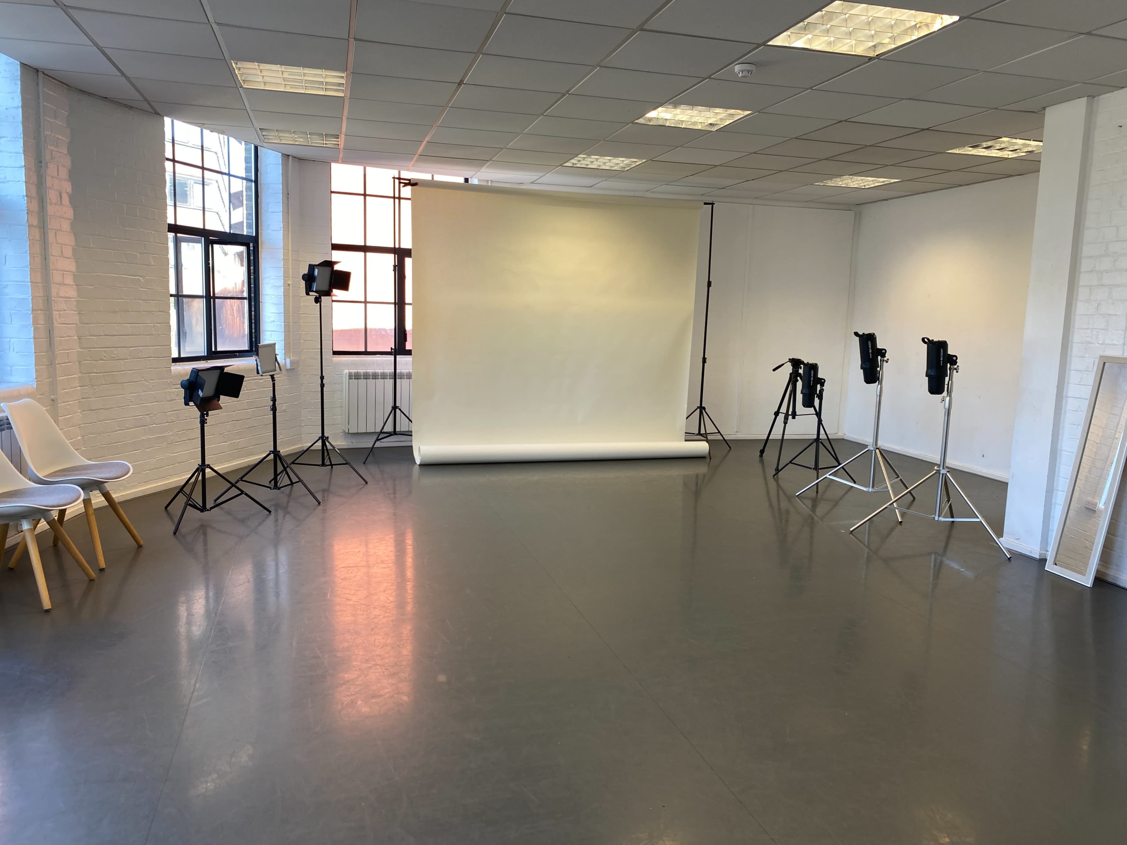A photography studio with a seamless backdrop, lighting equipment set up on stands, and minimalist seating in a spacious room.
