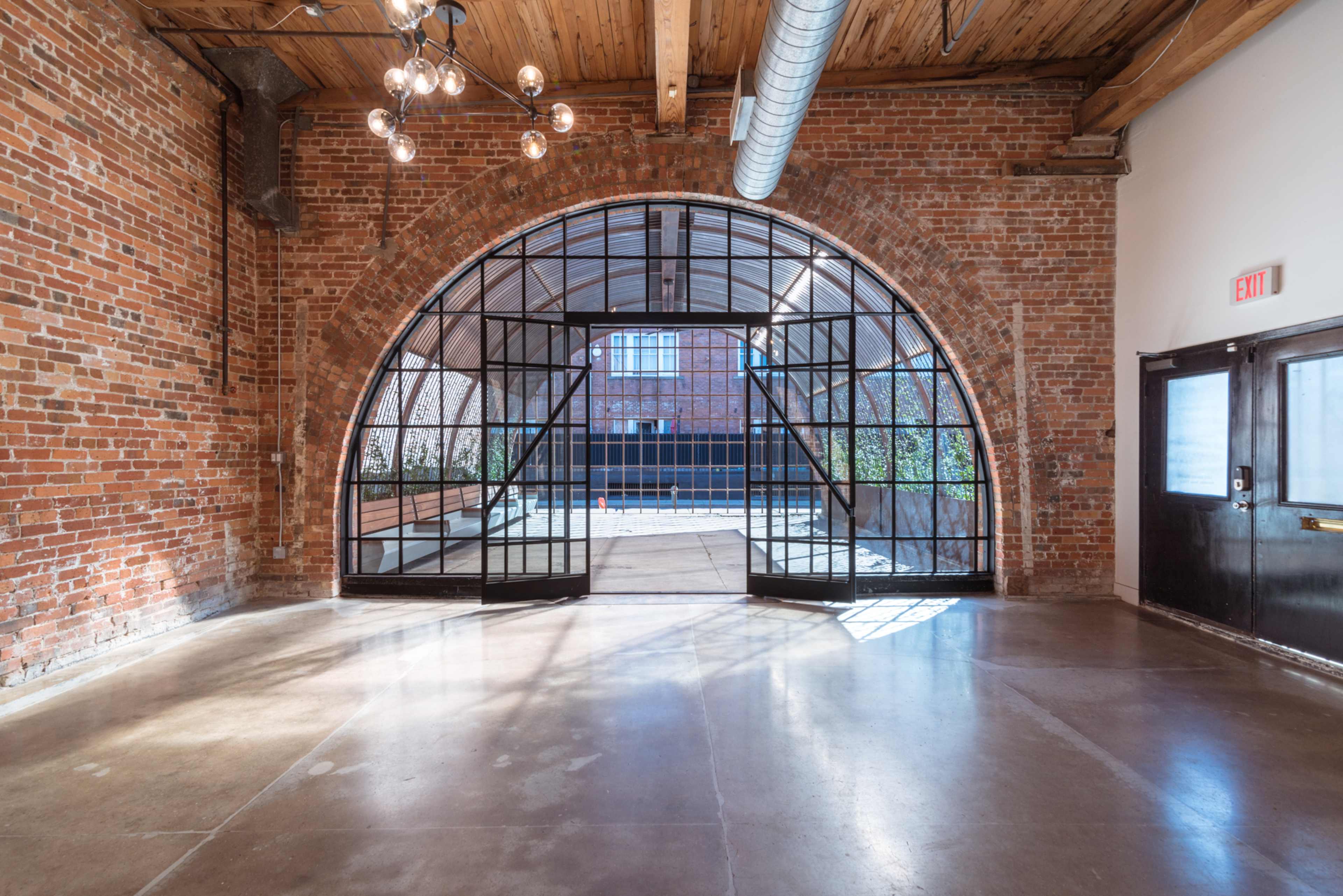 An expansive, brick-walled interior featuring a large arched glass door that leads to an outdoor area.