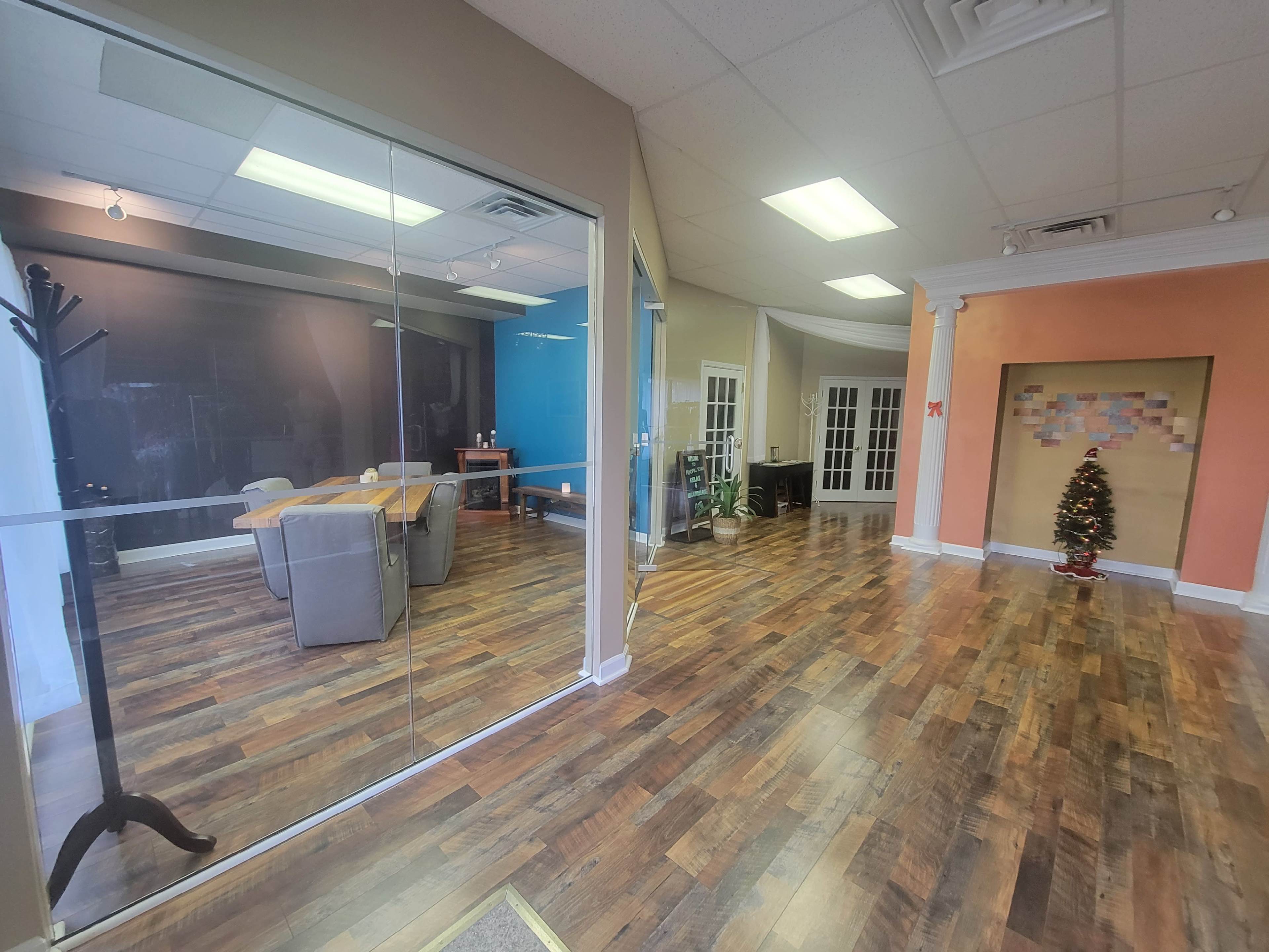 The image shows a spacious, divided office area with glass walls, featuring a conference table, chairs, and a decorative Christmas tree in the corner.