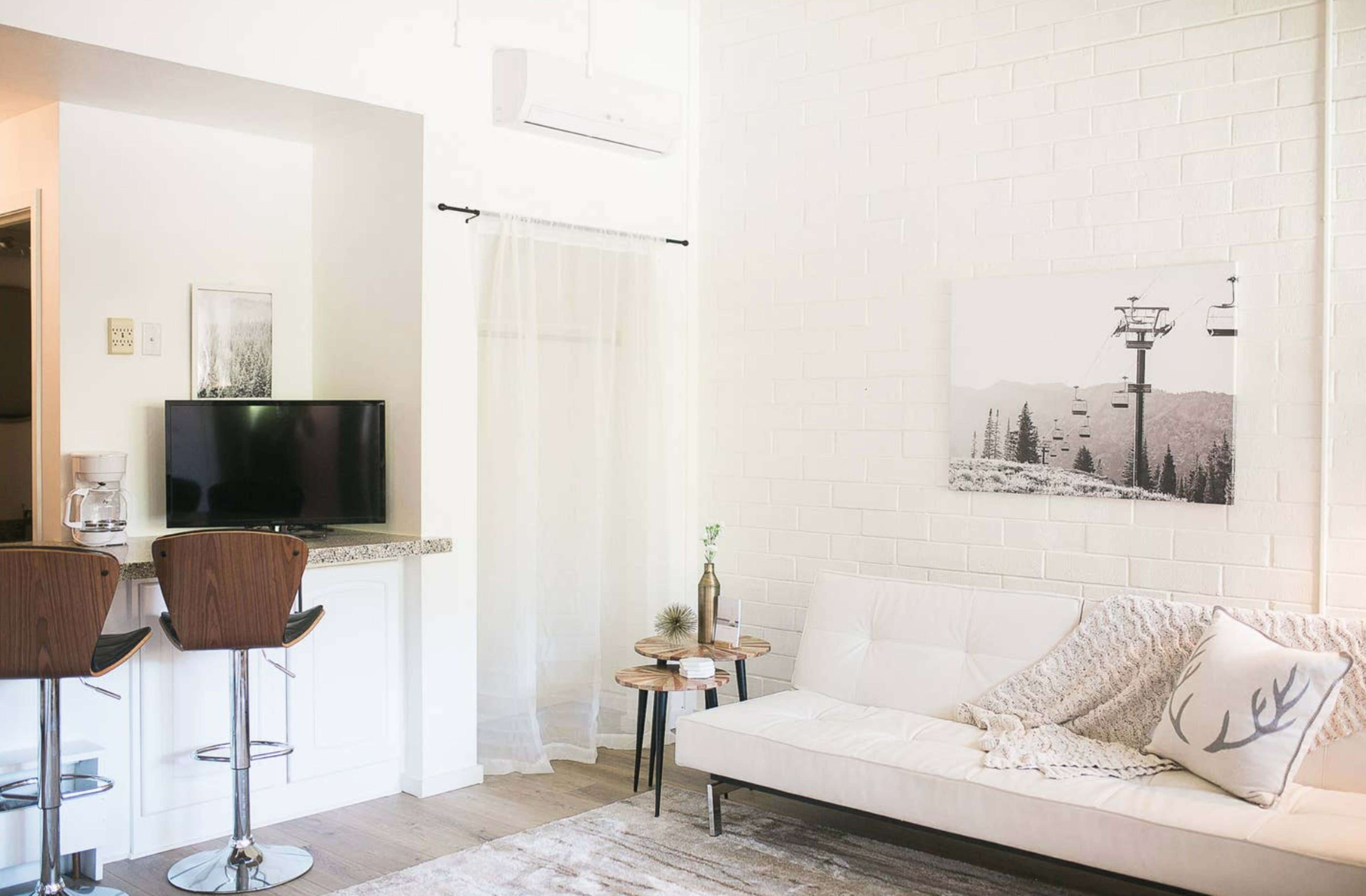 A modern living space with a white couch, a small round table, a television, and a wall featuring a mountain landscape photograph.