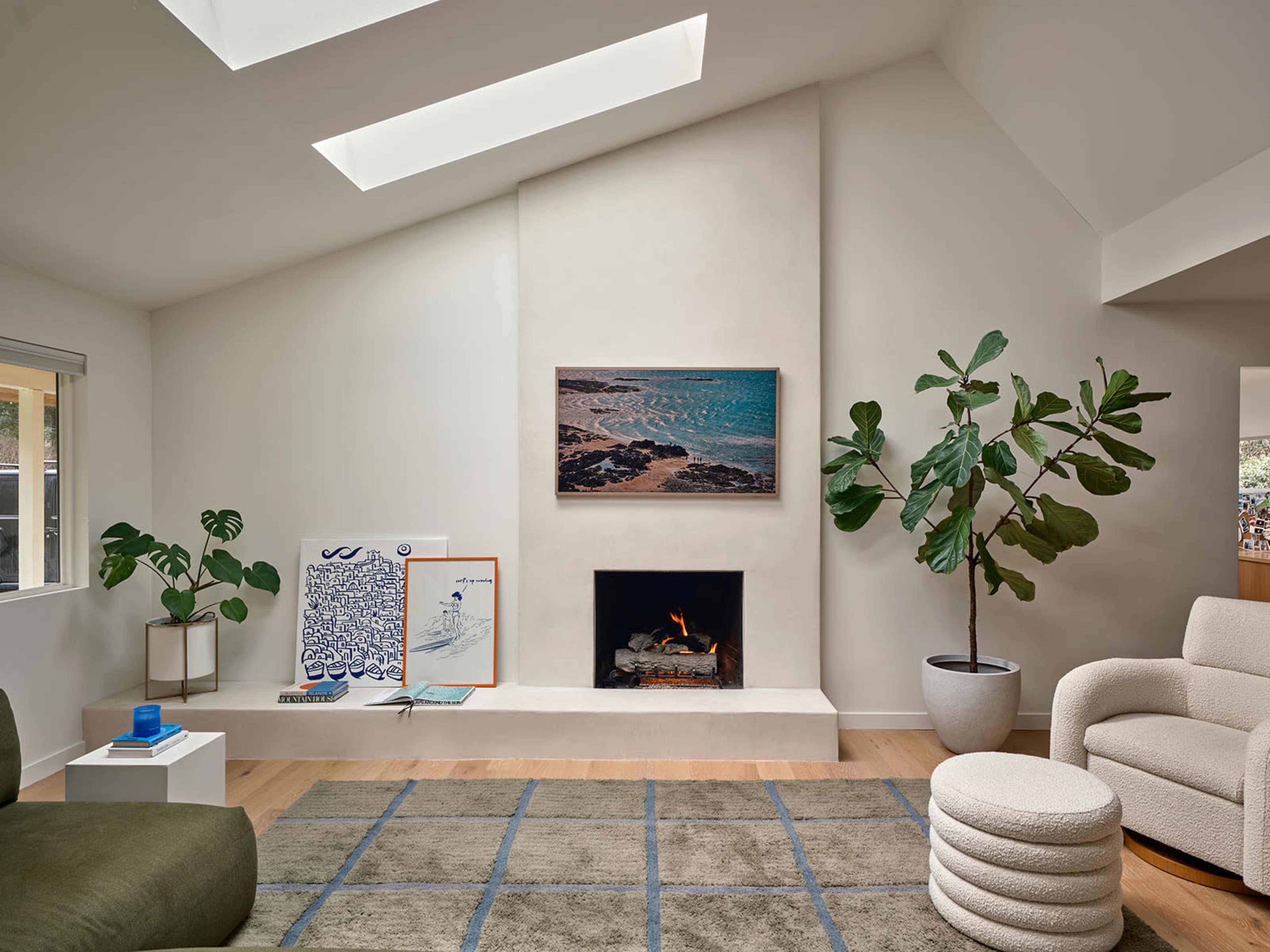 The image shows a modern living room featuring a fireplace, a large potted plant, and sectional seating, with artwork displayed on the walls.