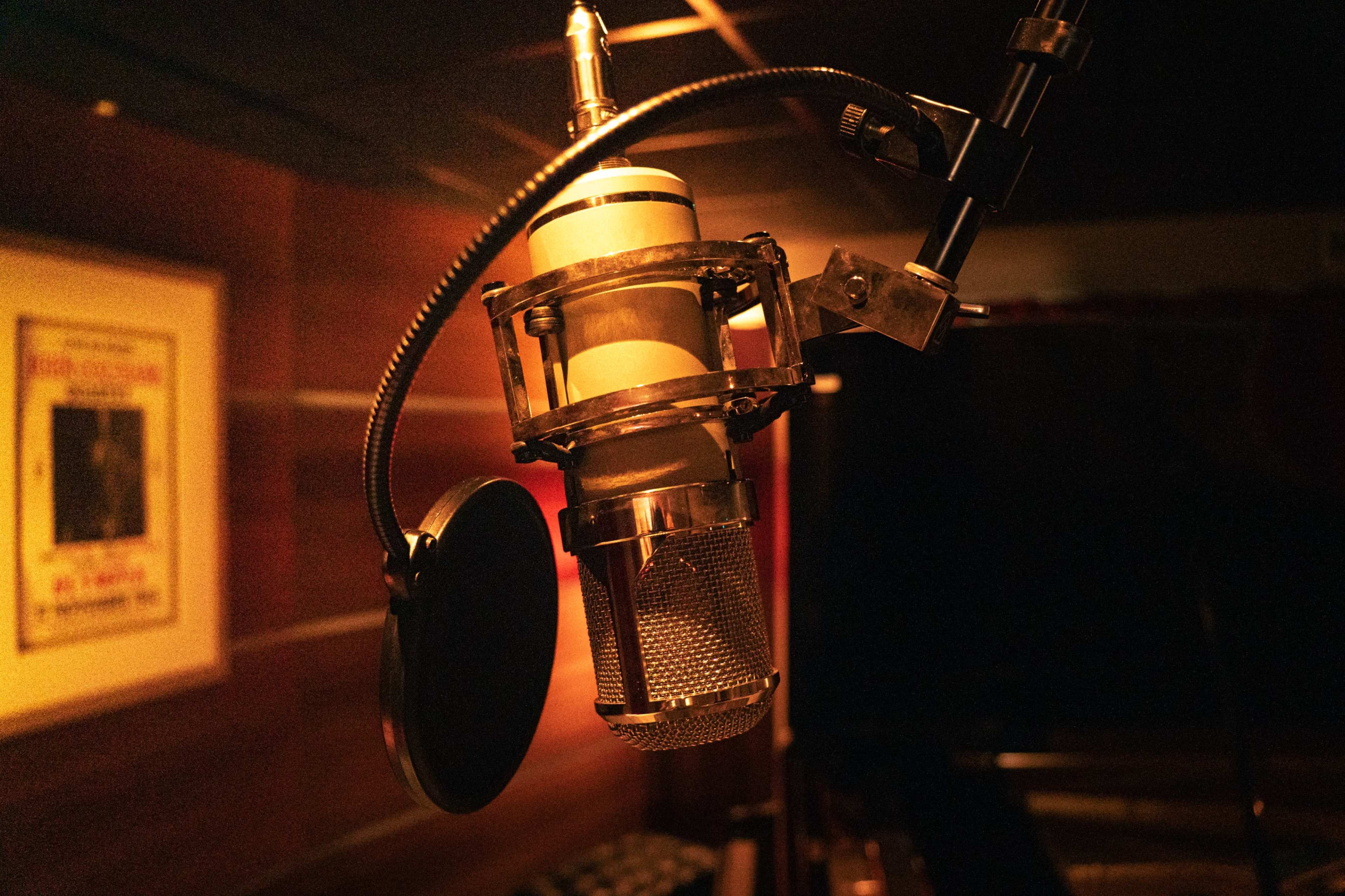 A vintage microphone is suspended on a boom arm in a dimly lit recording studio.