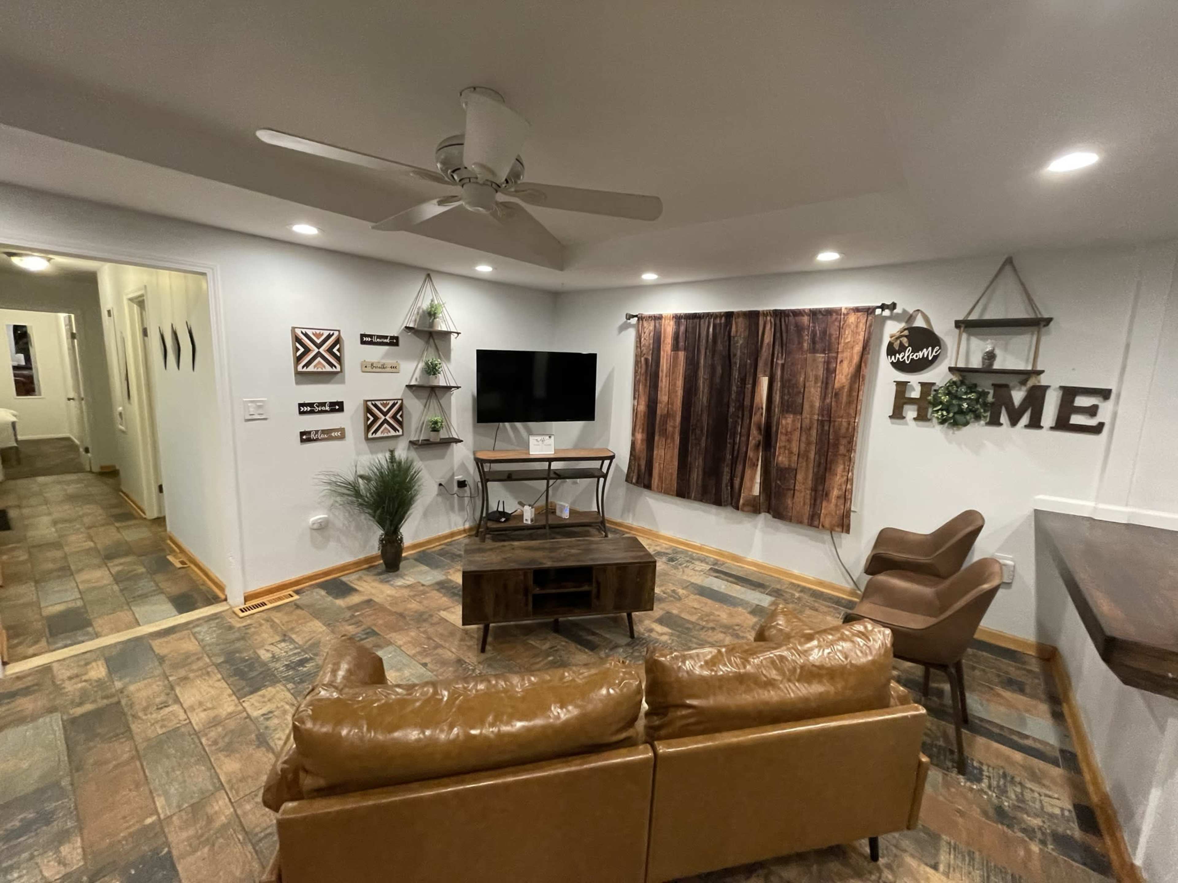 A cozy living room with a brown leather sofa, a wooden coffee table, a wall-mounted television, and rustic decor elements.