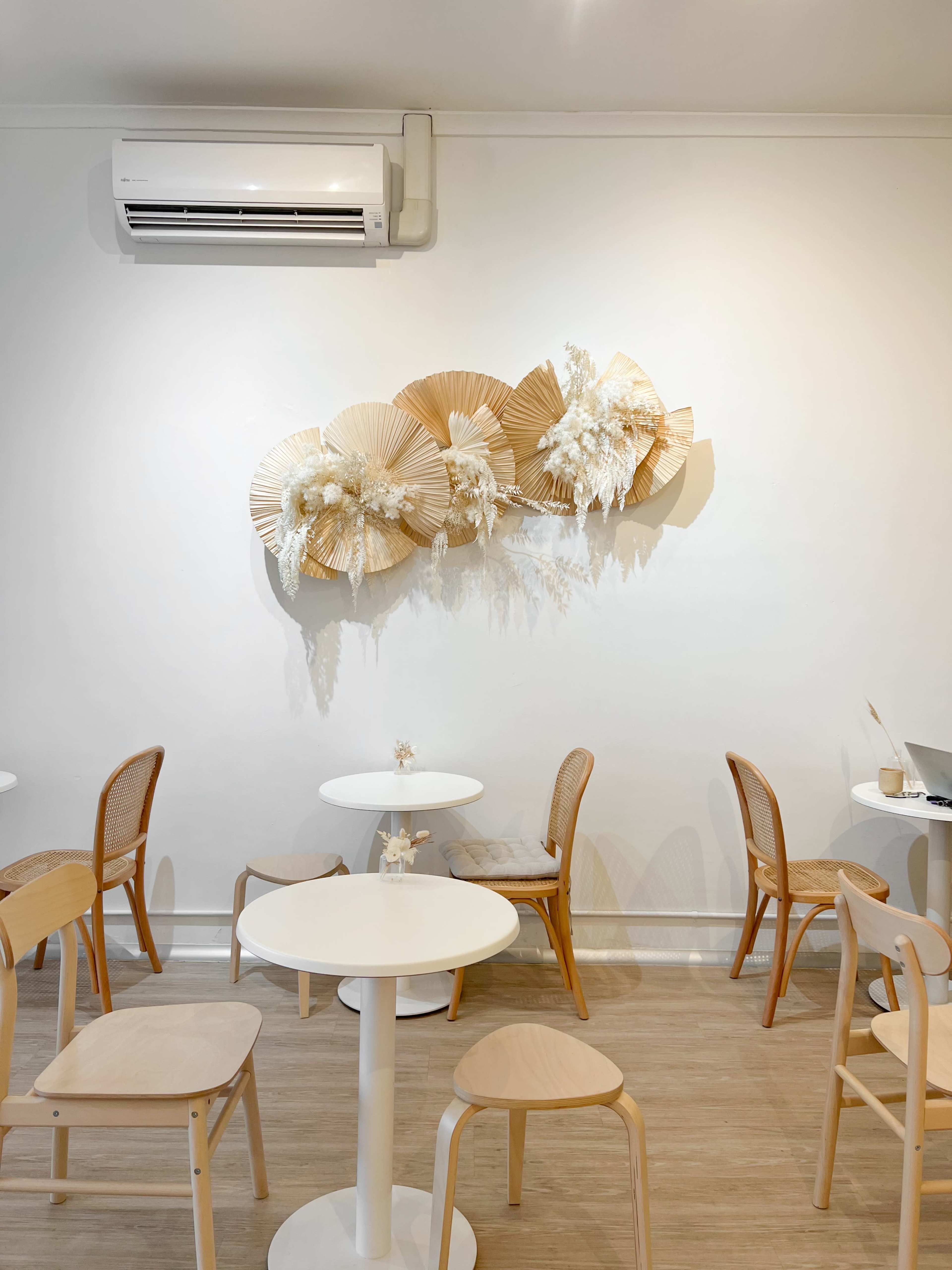 A minimalistic café interior featuring round tables and wooden chairs, with a decorative wall hanging made of natural materials.