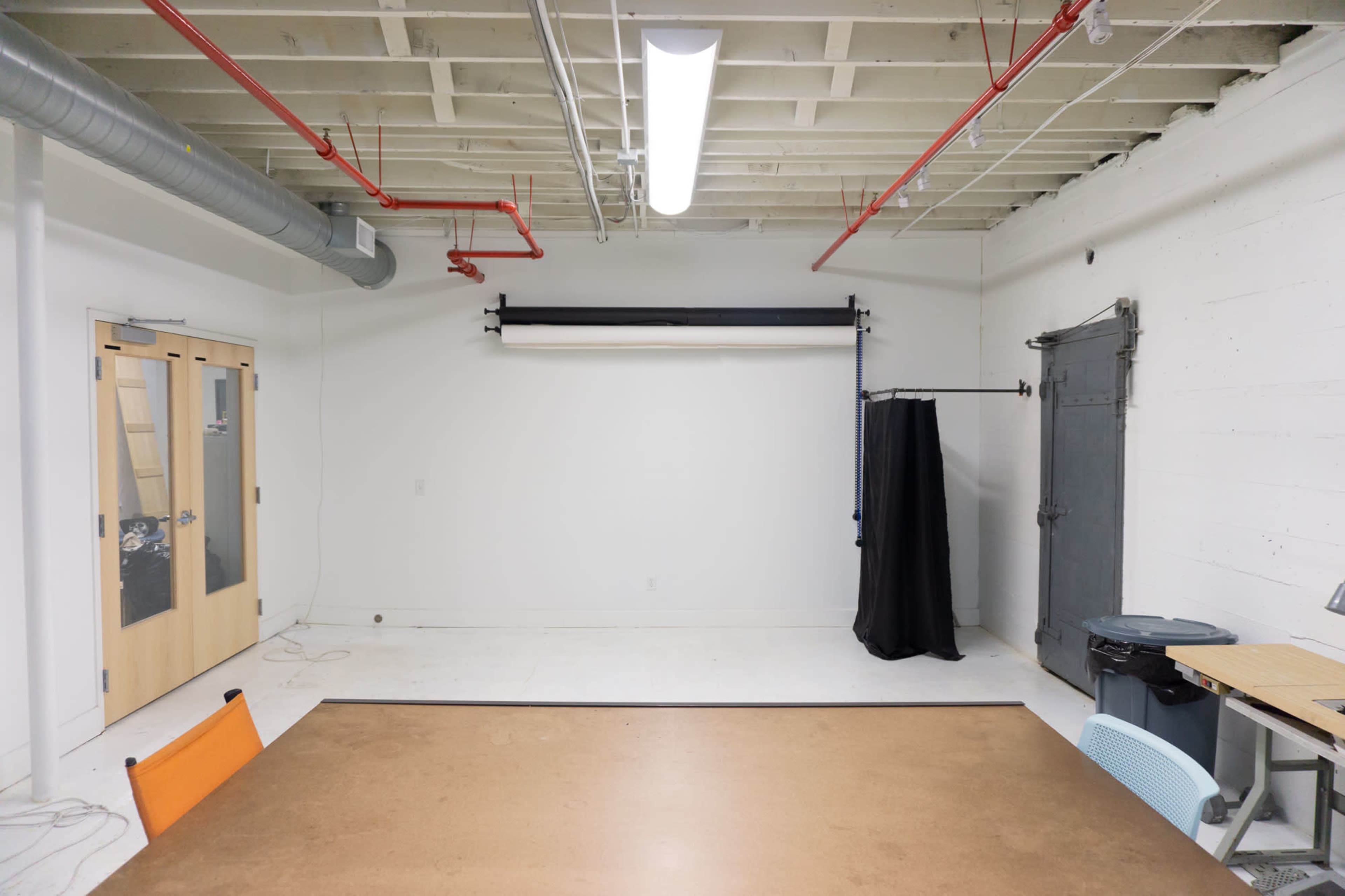 A minimalistic studio space with white walls, a large table in the foreground, and a backdrop setup against one wall.
