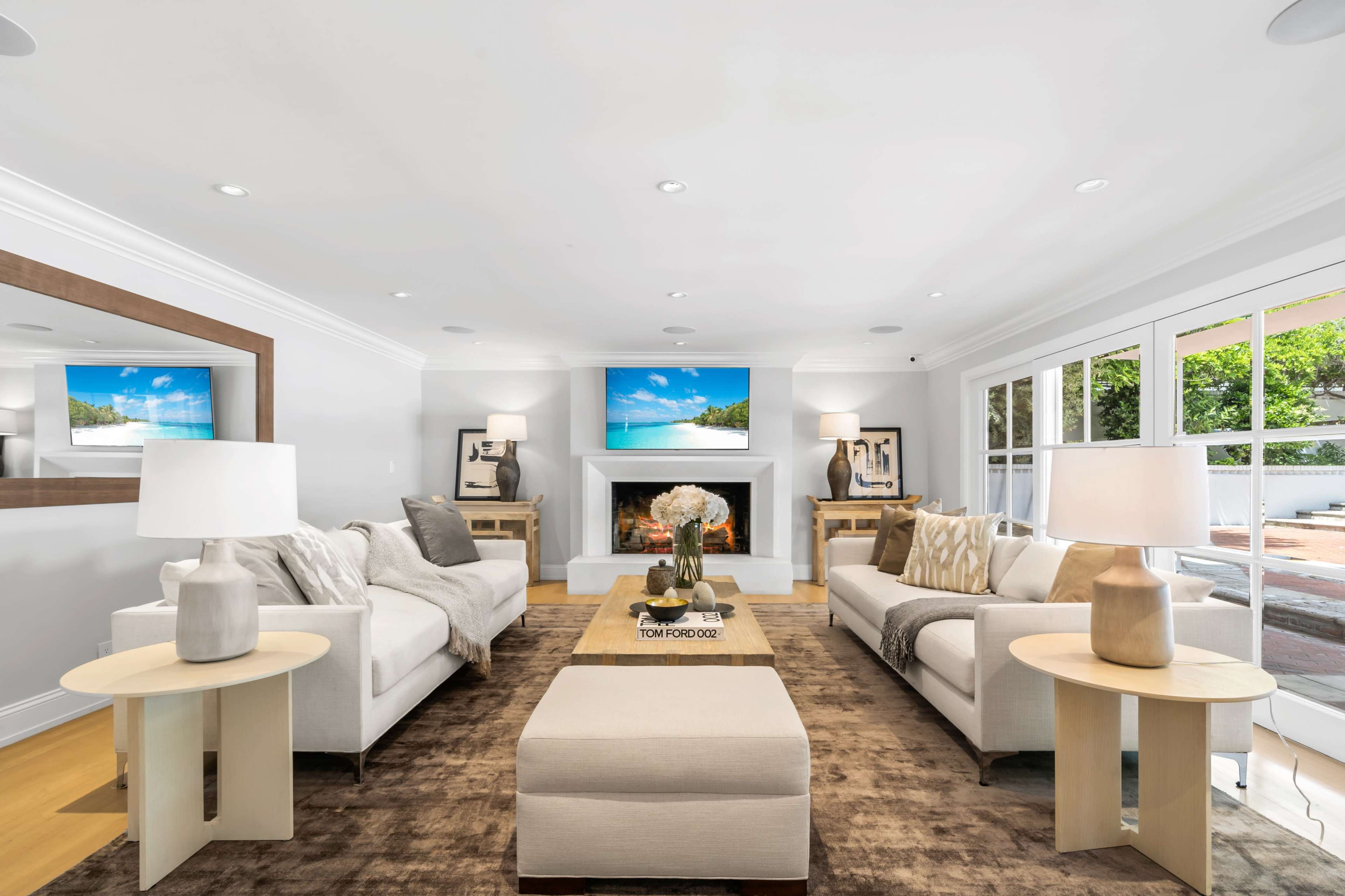 A modern living room featuring two light-colored sofas, a coffee table in the center, and a fireplace with a television mounted above it.