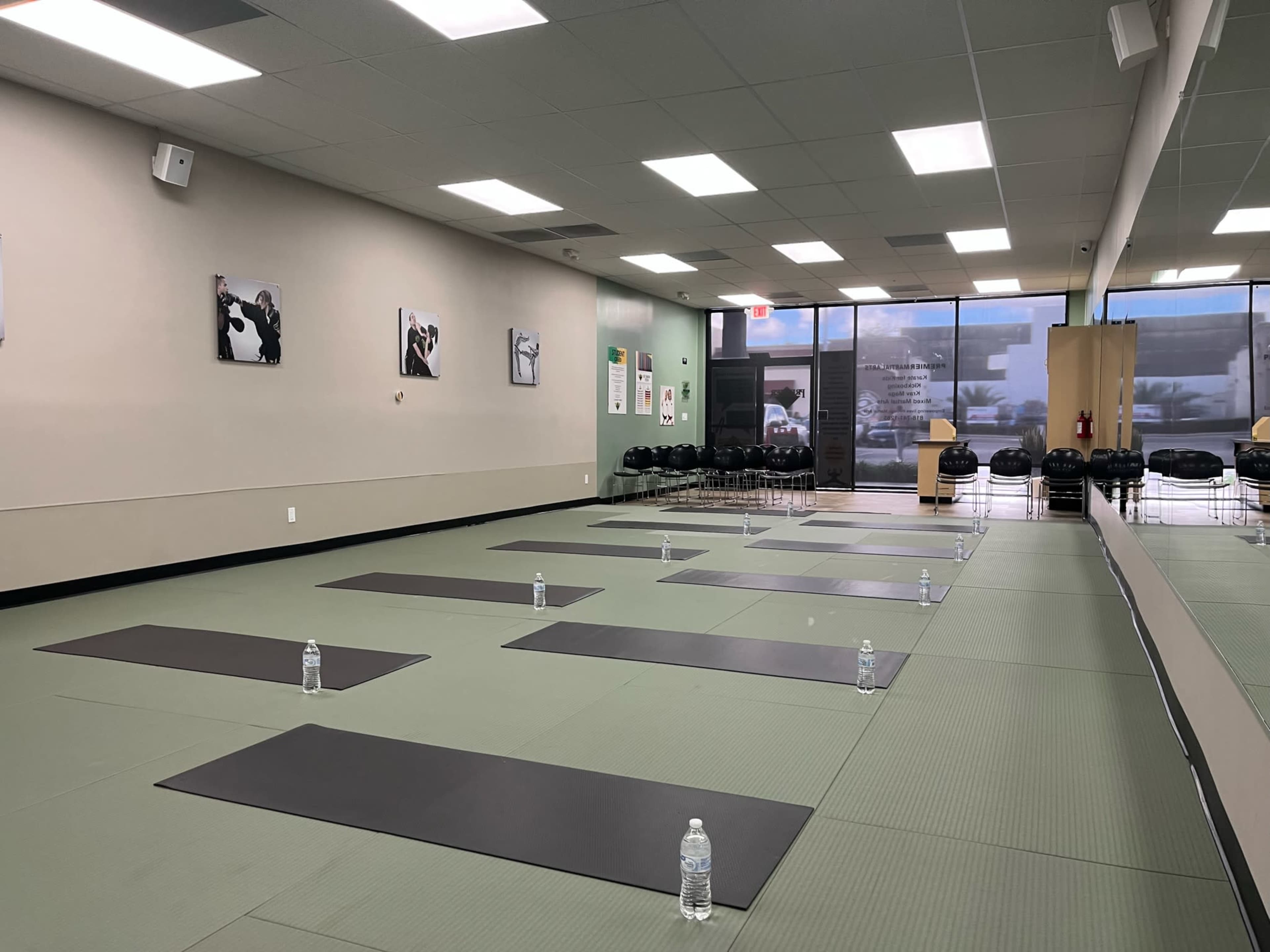 A yoga studio with several mats arranged on a green floor, each accompanied by a water bottle, and a large window providing natural light.