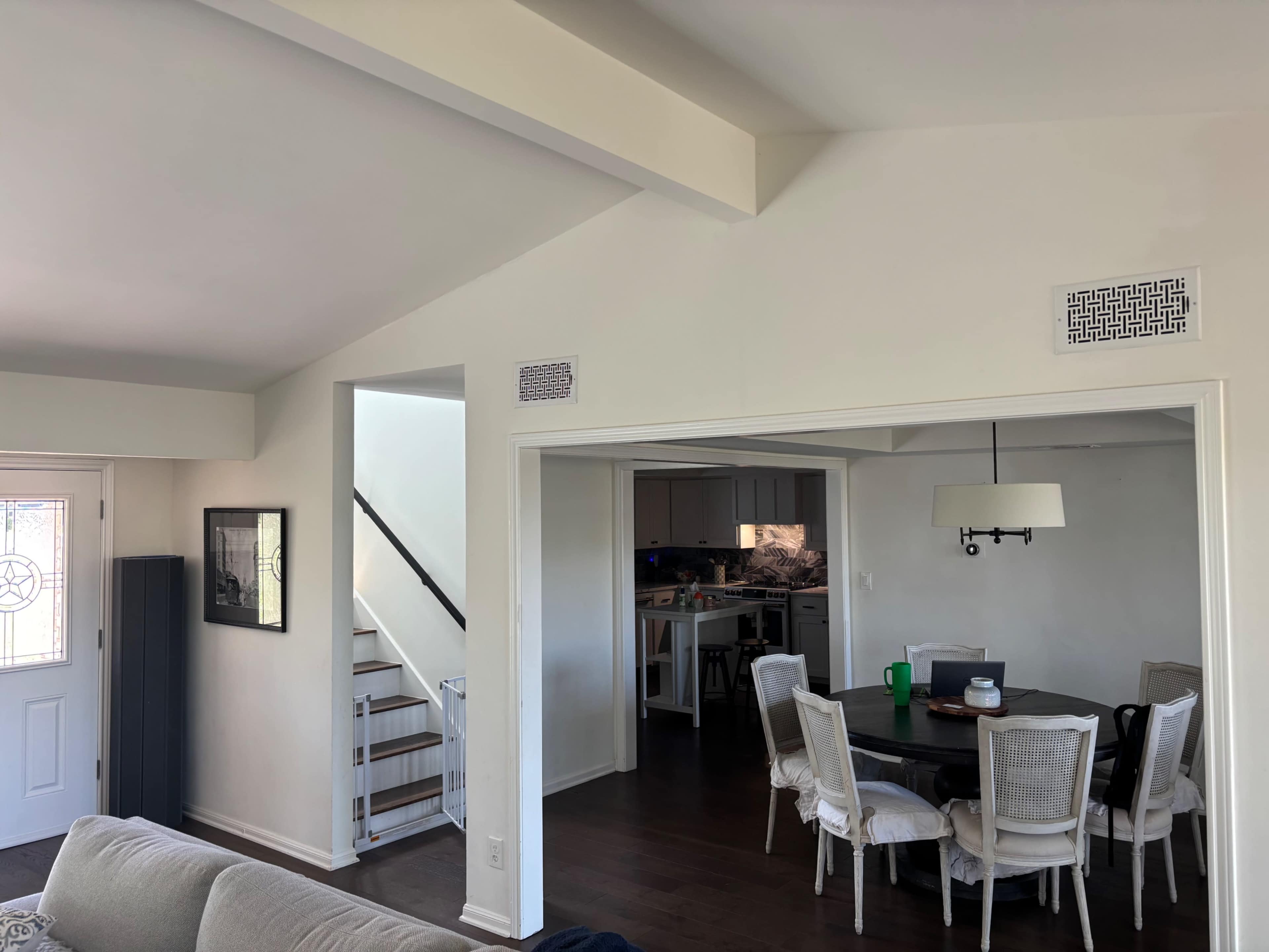 The image shows a bright interior space containing a living area with a couch, a dining table, and a staircase leading to an upper level.