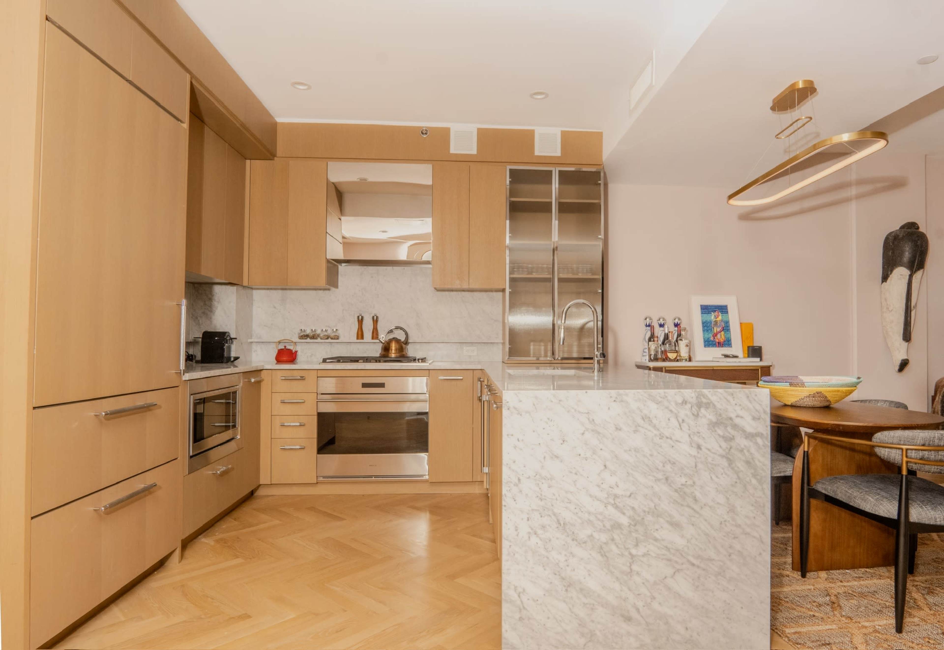 The image shows a modern kitchen with wooden cabinetry, a marble island, and an adjoining dining area.