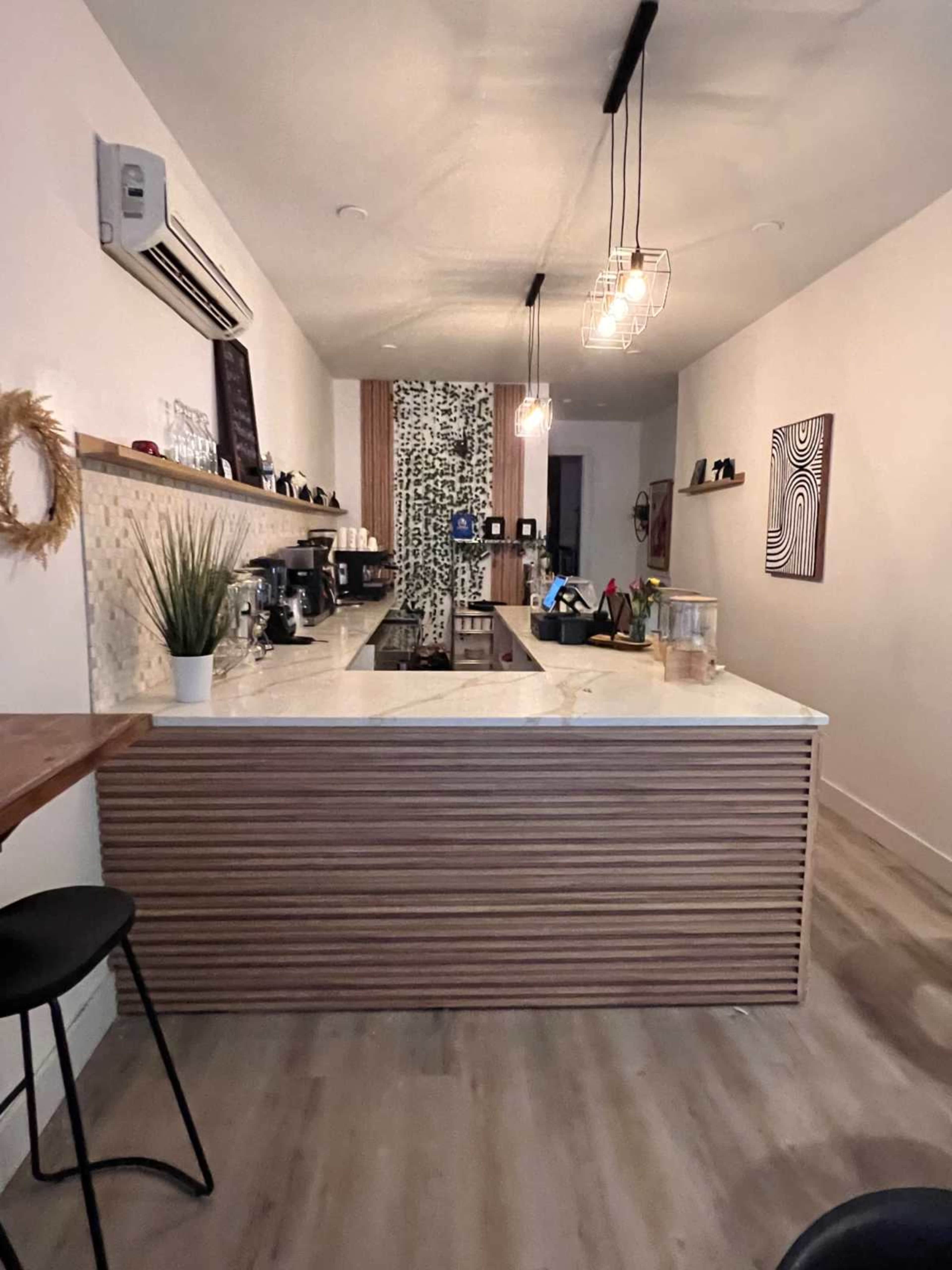 The image depicts a modern kitchen featuring a central island with a marble countertop, wooden cabinetry, and wall decor that includes a patterned backsplash.