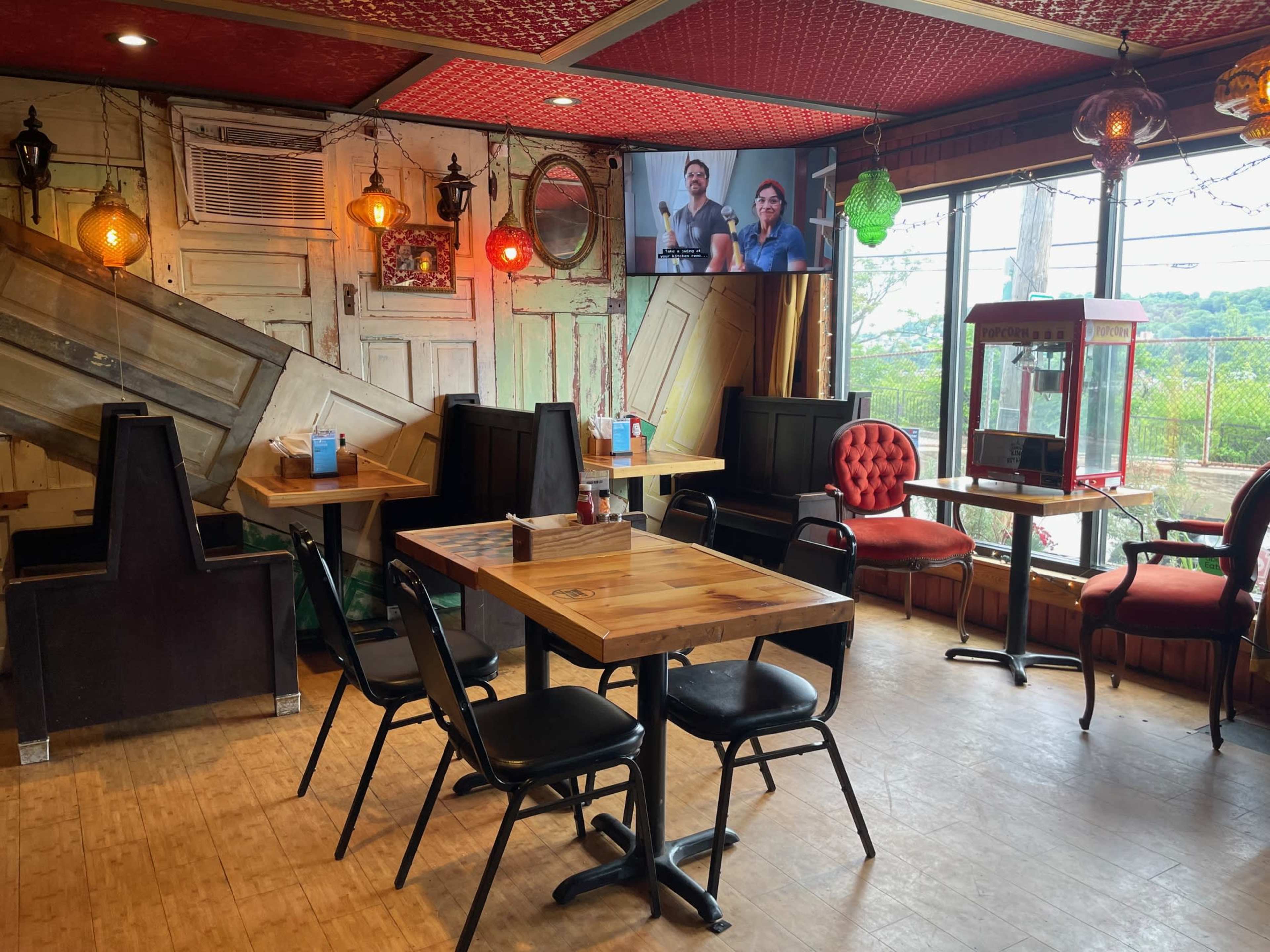 The image shows a cozy restaurant interior with wooden tables, black chairs, and vintage decorations, including a popcorn machine and a television on the wall.