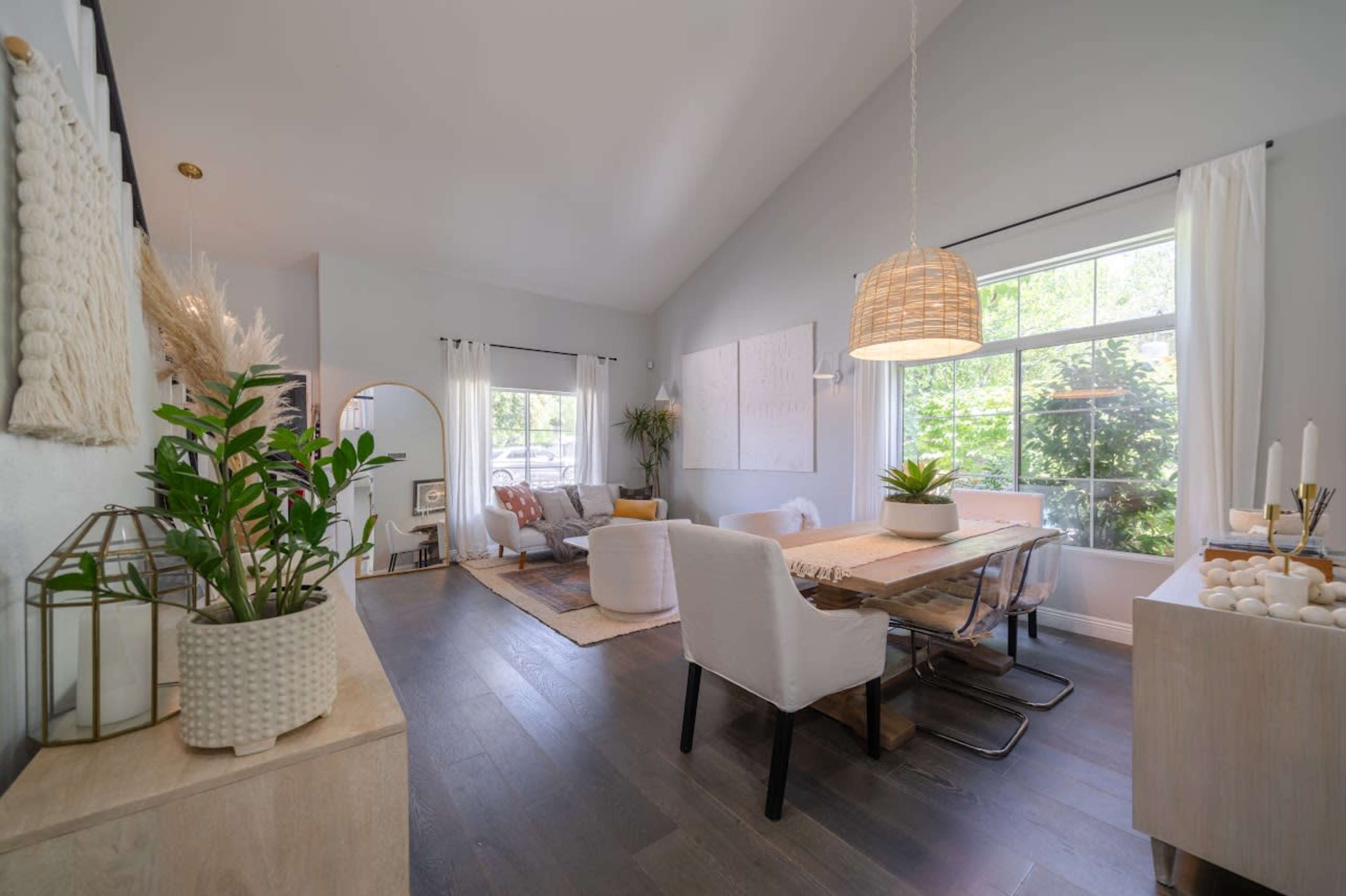 A spacious living area features a dining table, comfortable seating, and large windows allowing natural light to enter.