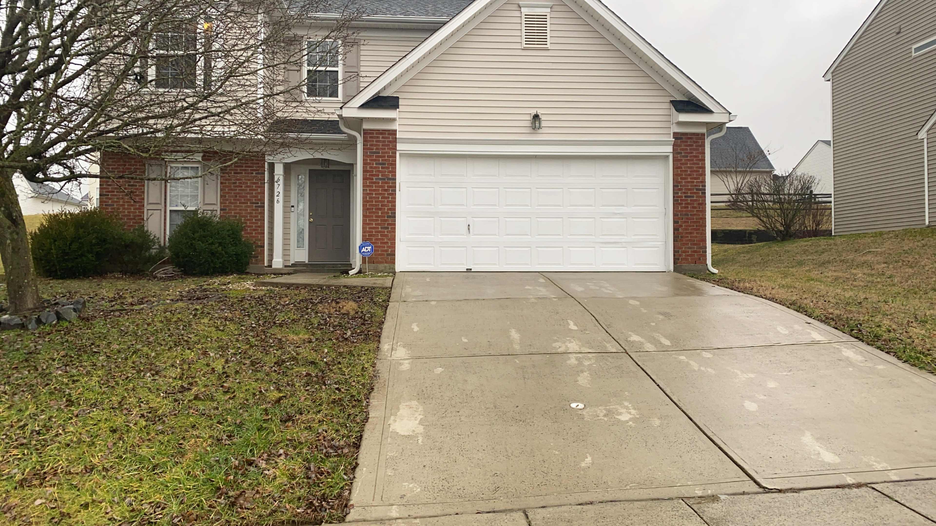 A suburban house features a two-car garage with a concrete driveway and a lawn partially covered in grass.
