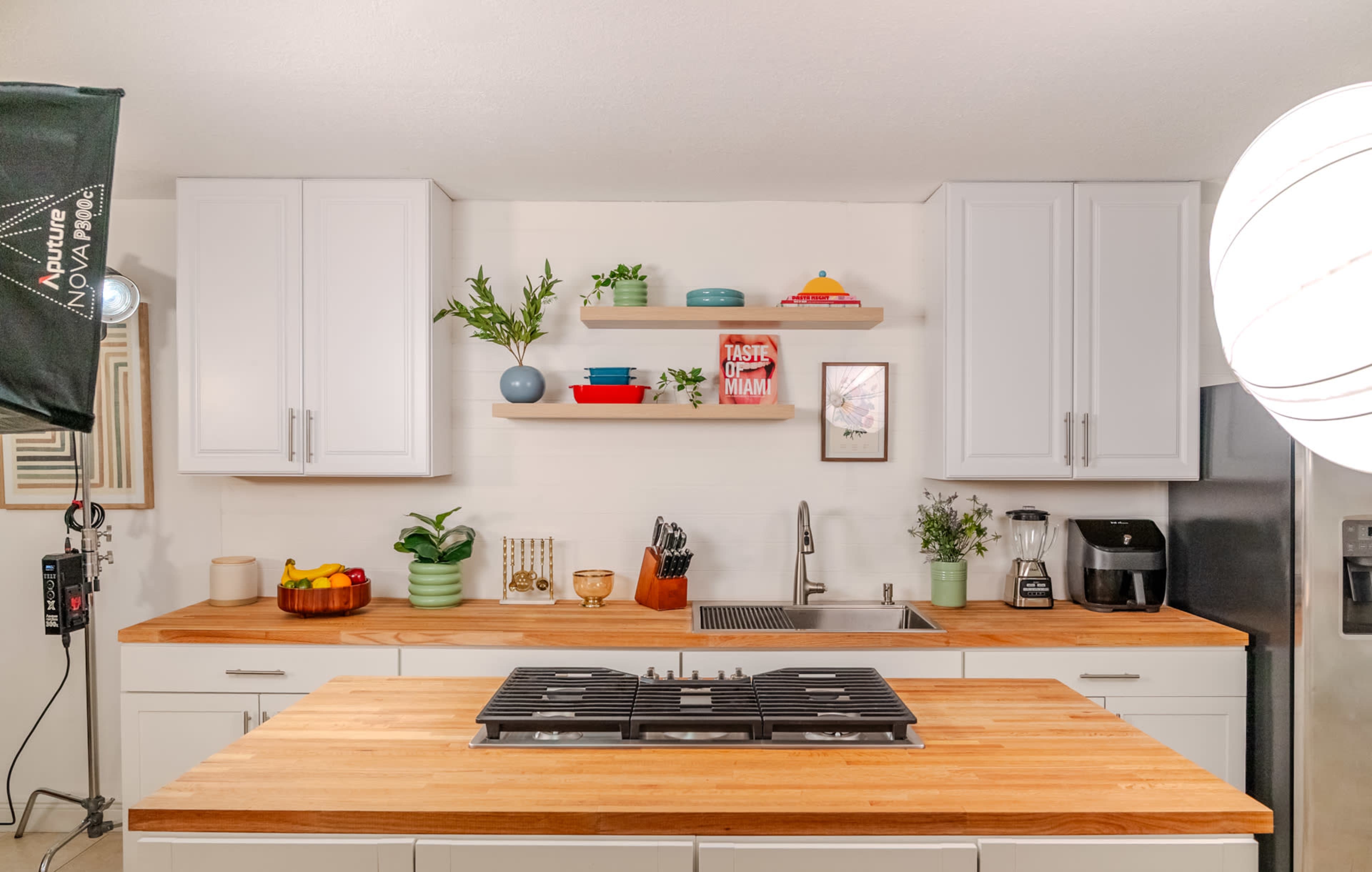 The image shows a modern kitchen with white cabinets, a wooden countertop, and a central island featuring a stovetop.