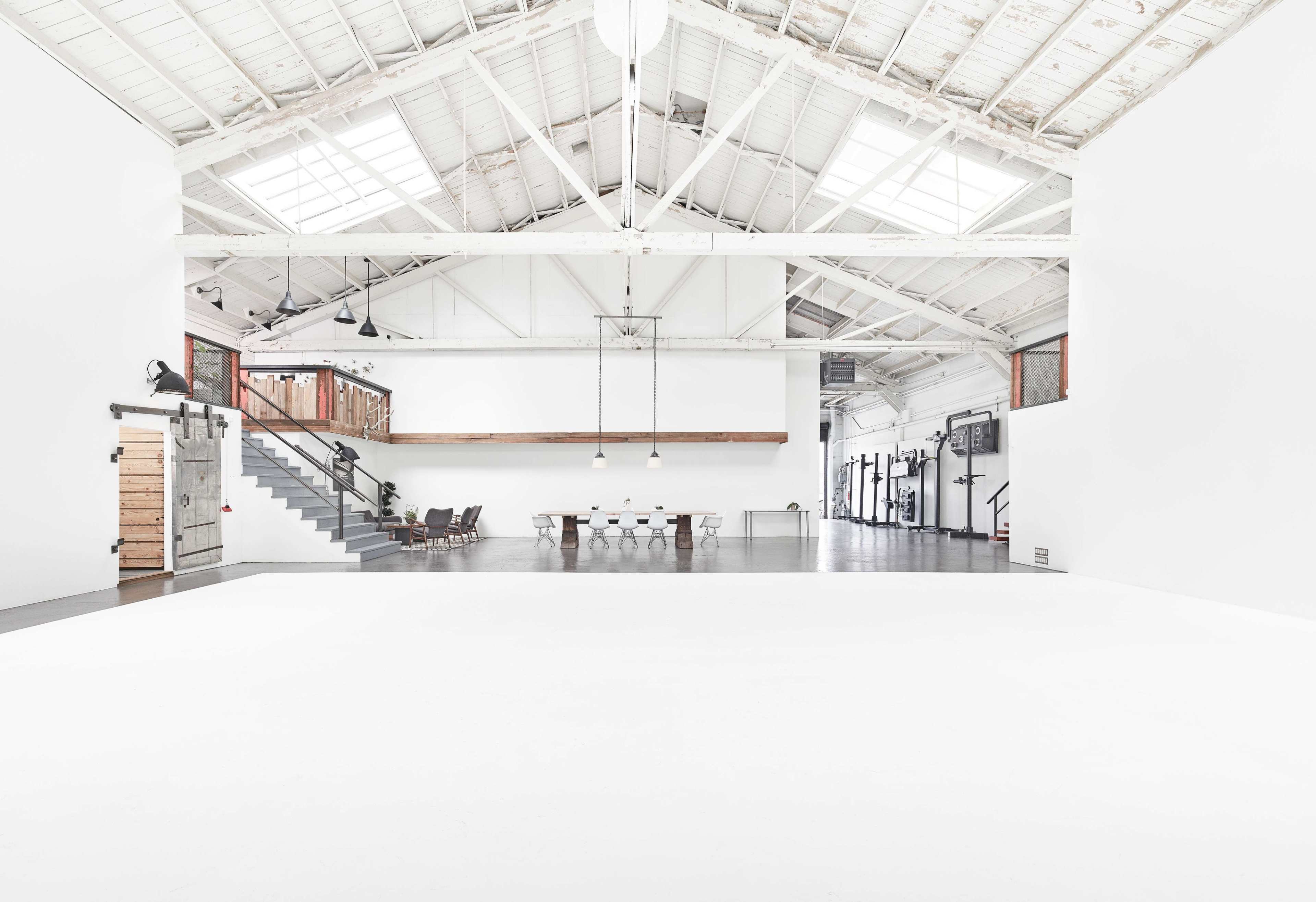 A spacious, industrial-style interior with high ceilings, white walls, and a staircase leading to an upper level.