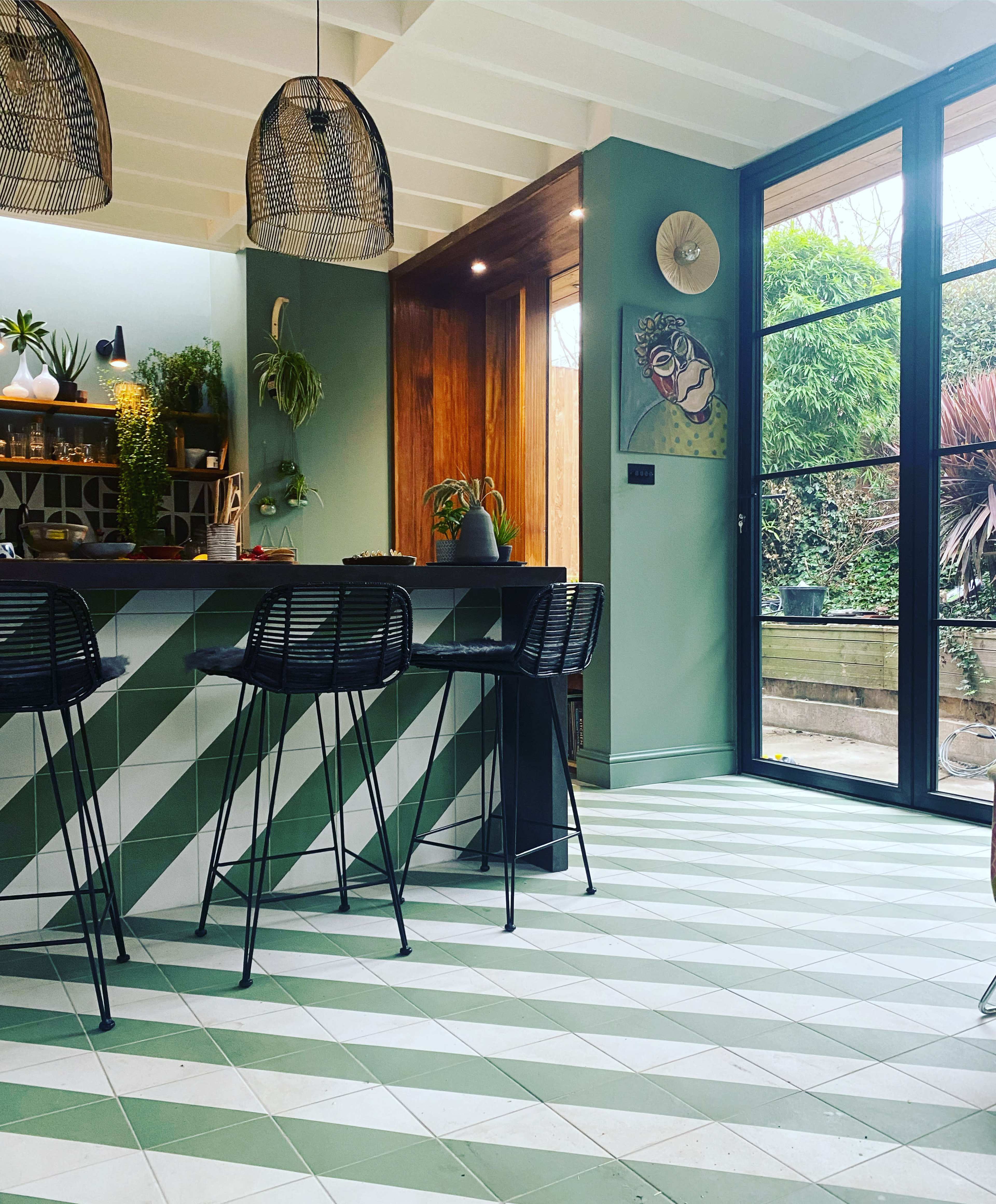 A modern kitchen with a green and white tiled floor, a bar area with black bar stools, and large glass doors leading to an outdoor space.