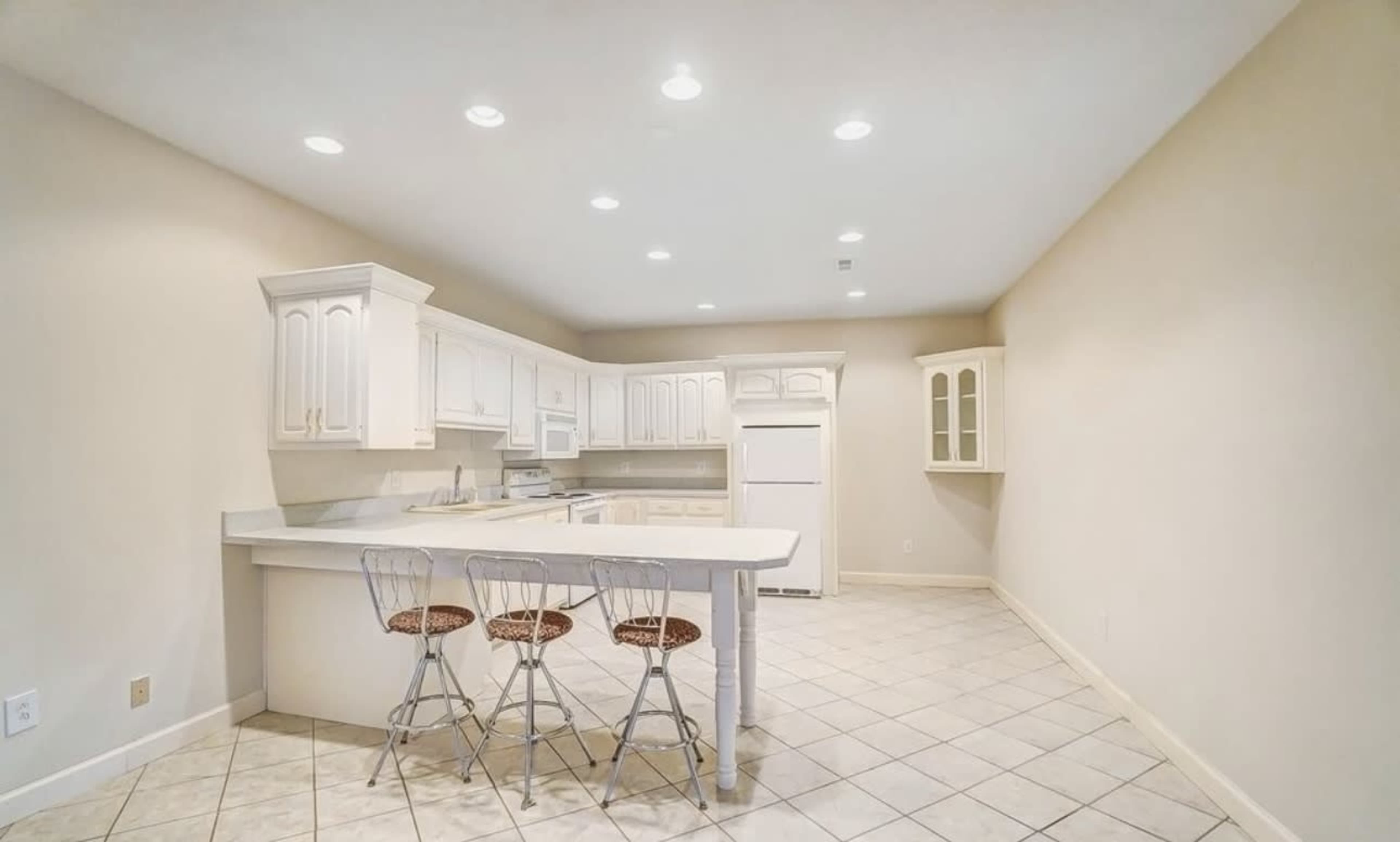 The image showcases a spacious kitchen featuring white cabinets, a central island with bar stools, and tiled flooring.