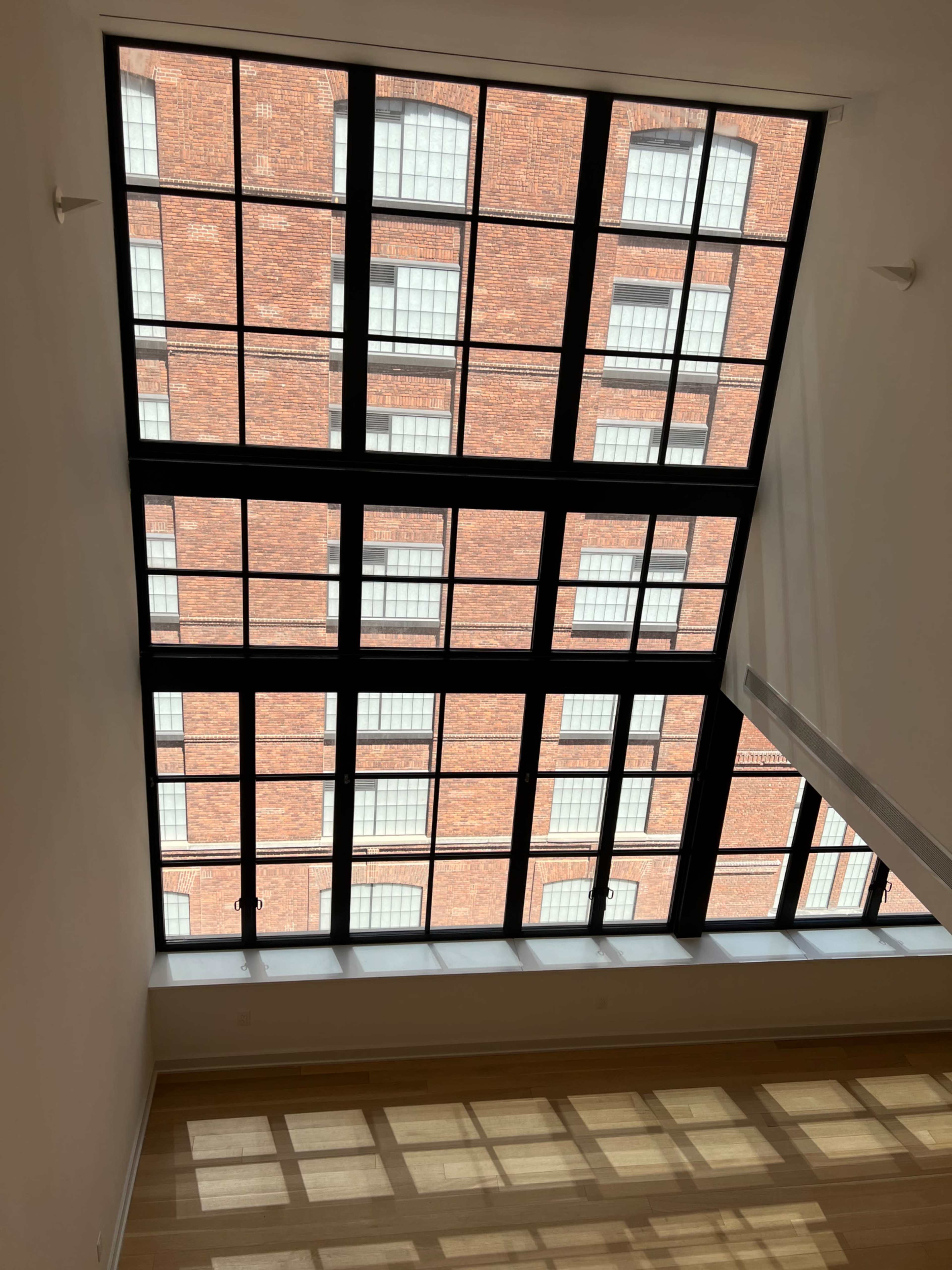 The image shows a large window with a grid pattern overlooking a brick building.
