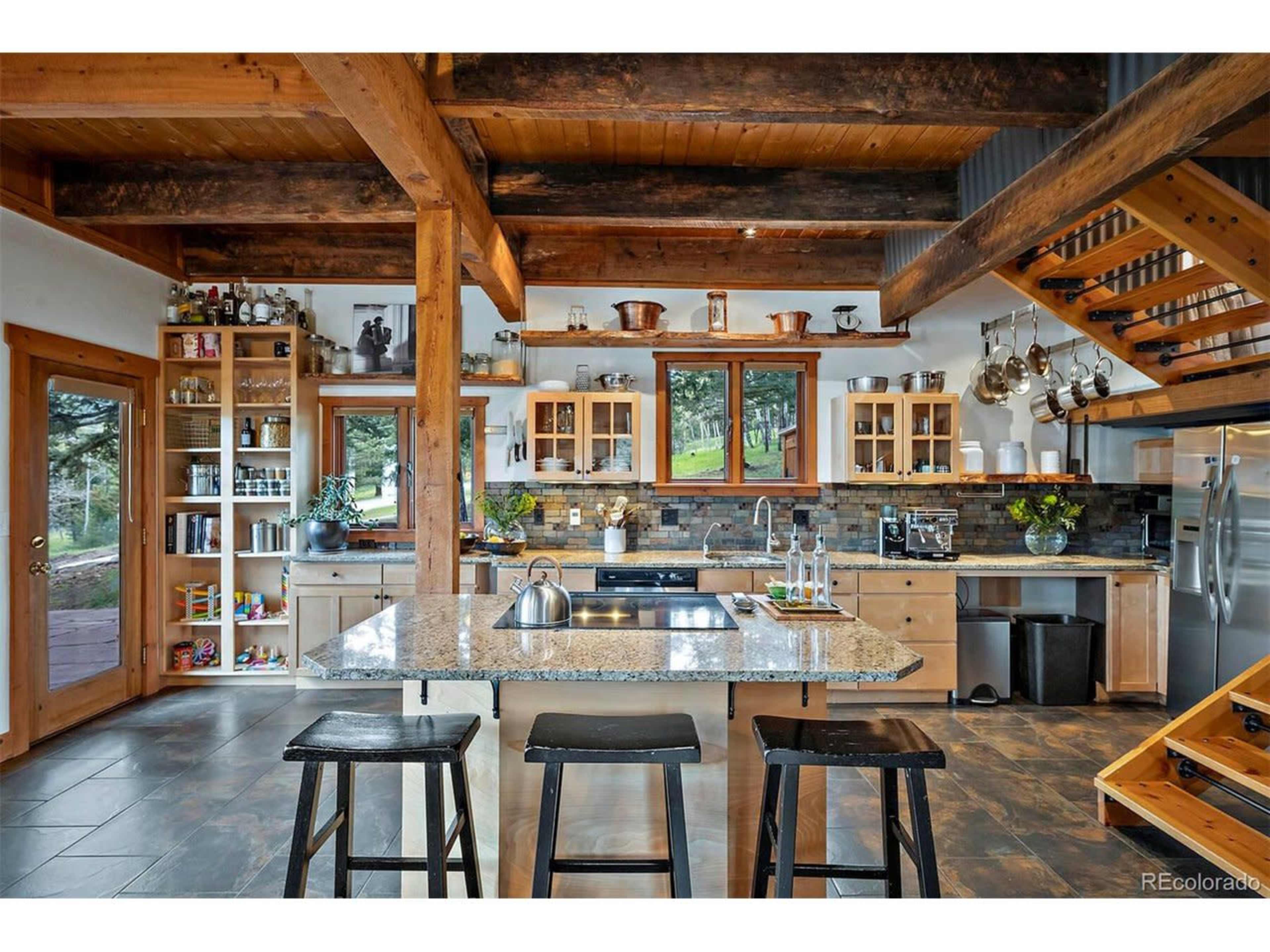 A modern kitchen features wooden beams, a central island with seating, and various kitchen appliances and utensils arranged on shelves.