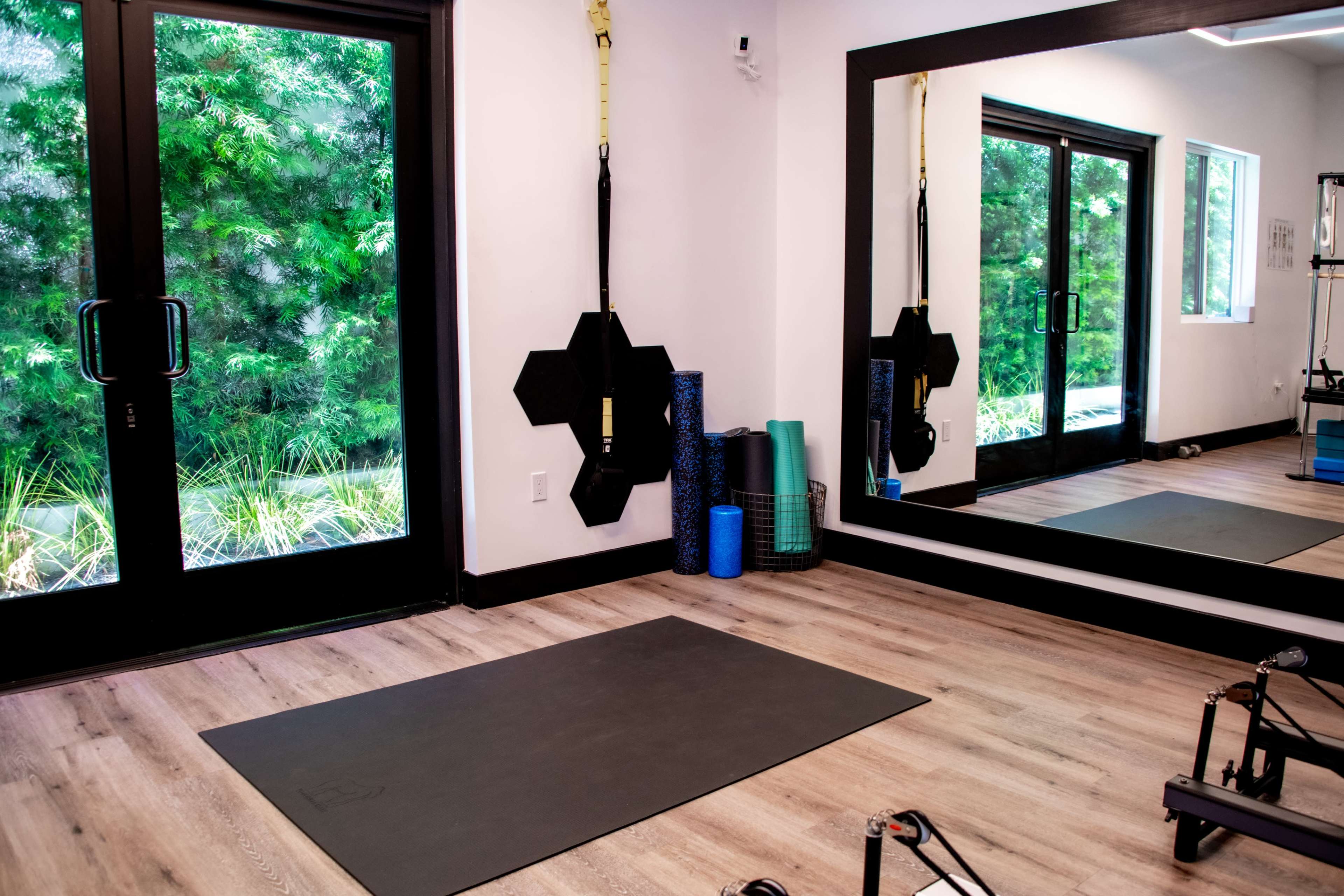 A minimalist home gym with a mat on the floor, exercise mats rolled up against the wall, and large windows overlooking greenery.