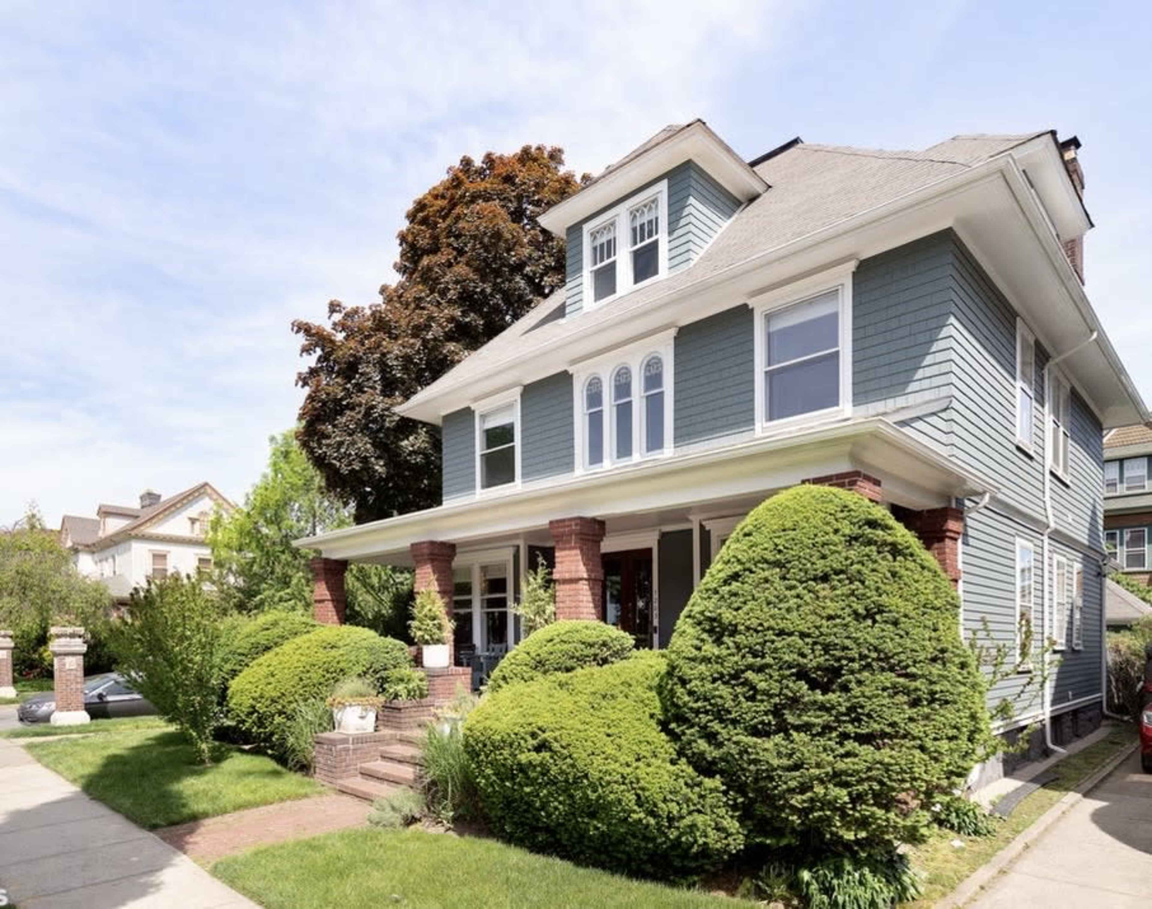 A three-story blue house with white trim, surrounded by well-maintained shrubs and trees.