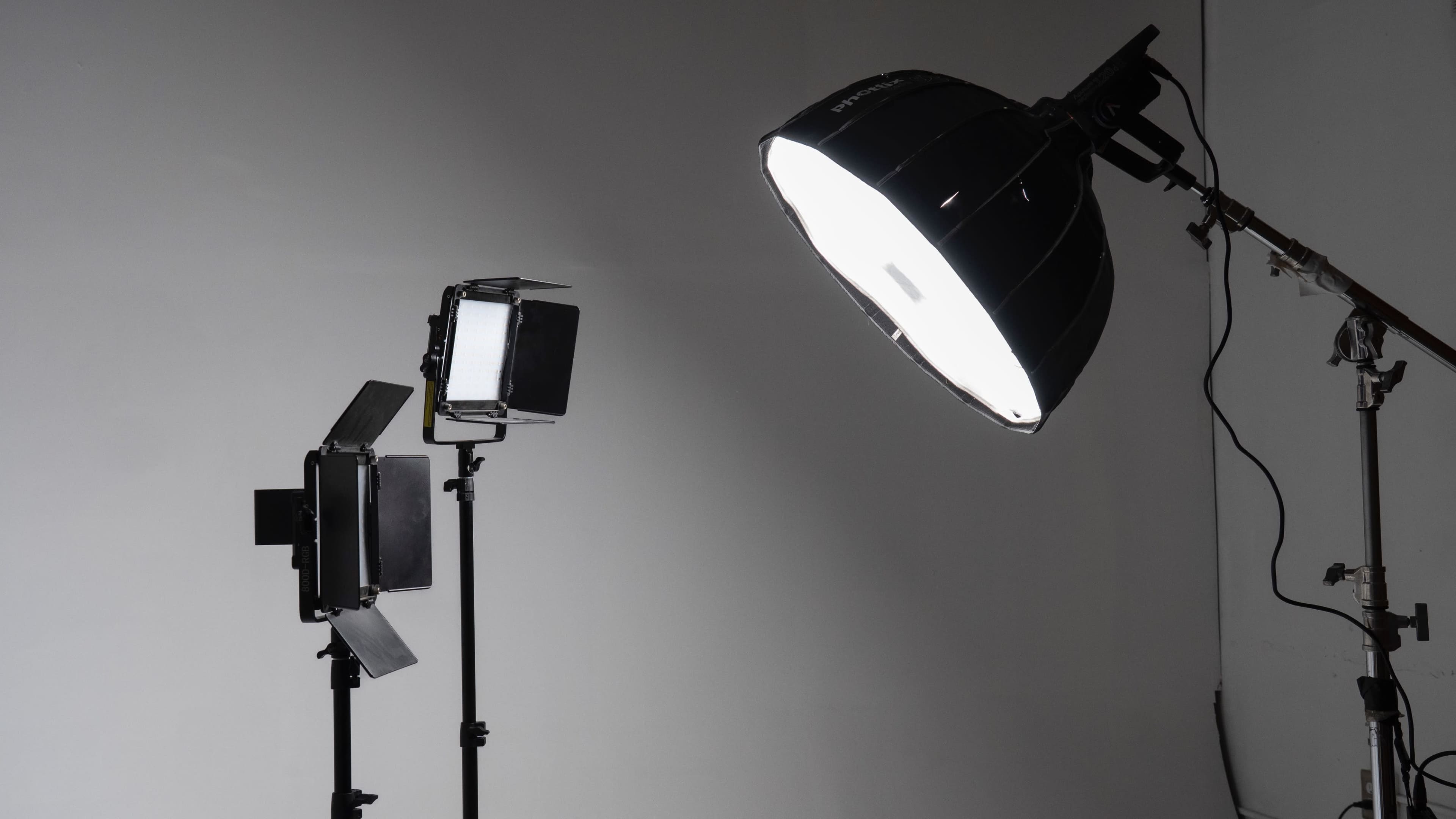 The image shows two studio lights on stands, one with a softbox and the other with a reflective umbrella, set against a plain white backdrop.