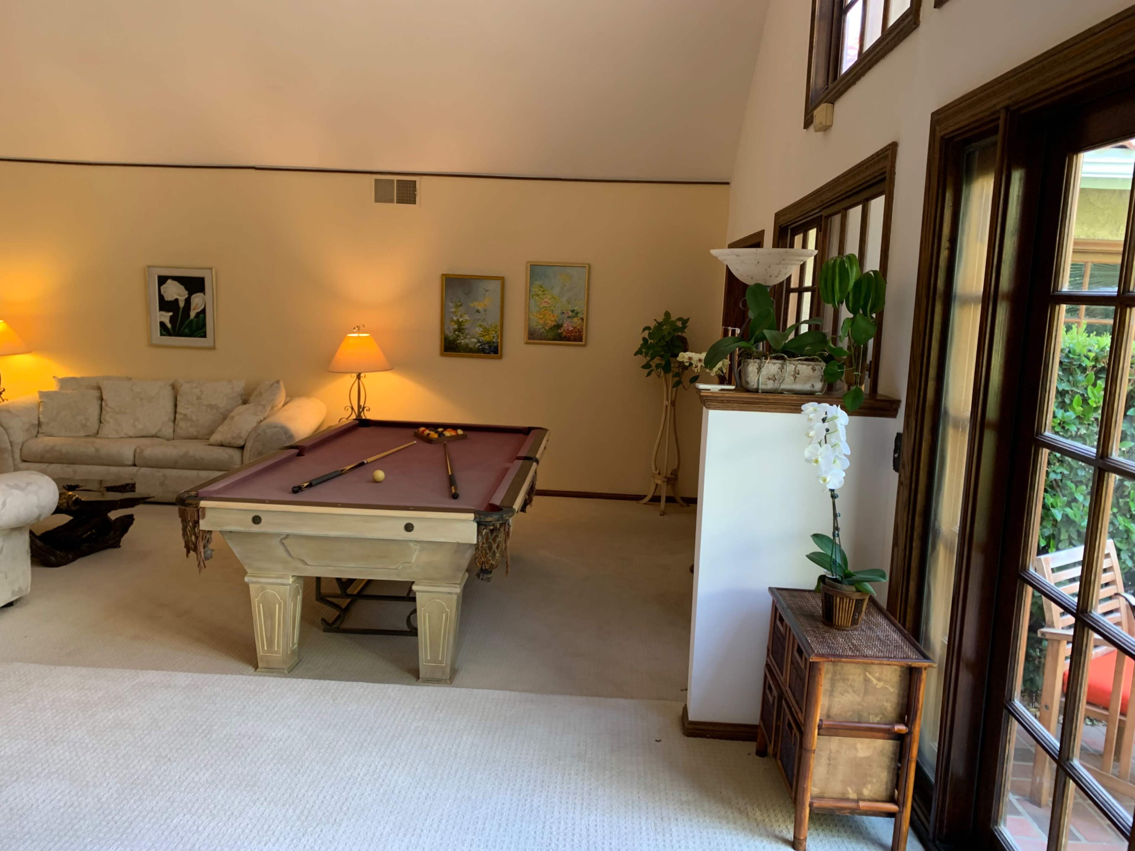 The room features a pool table in the center, surrounded by a sofa, lamps, and artwork on the walls.
