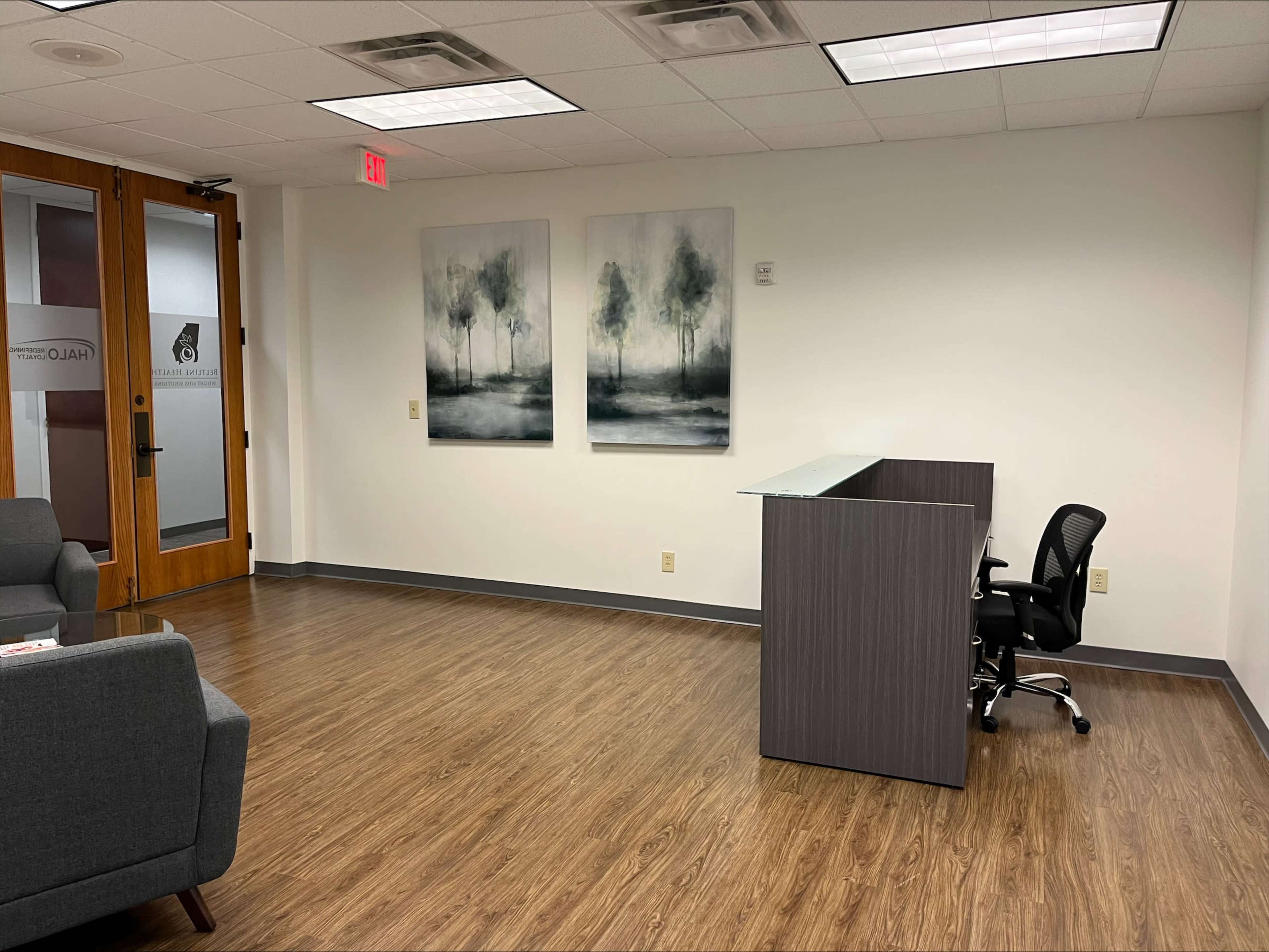 A modern office reception area with a desk, a chair, and two large abstract paintings on the wall.