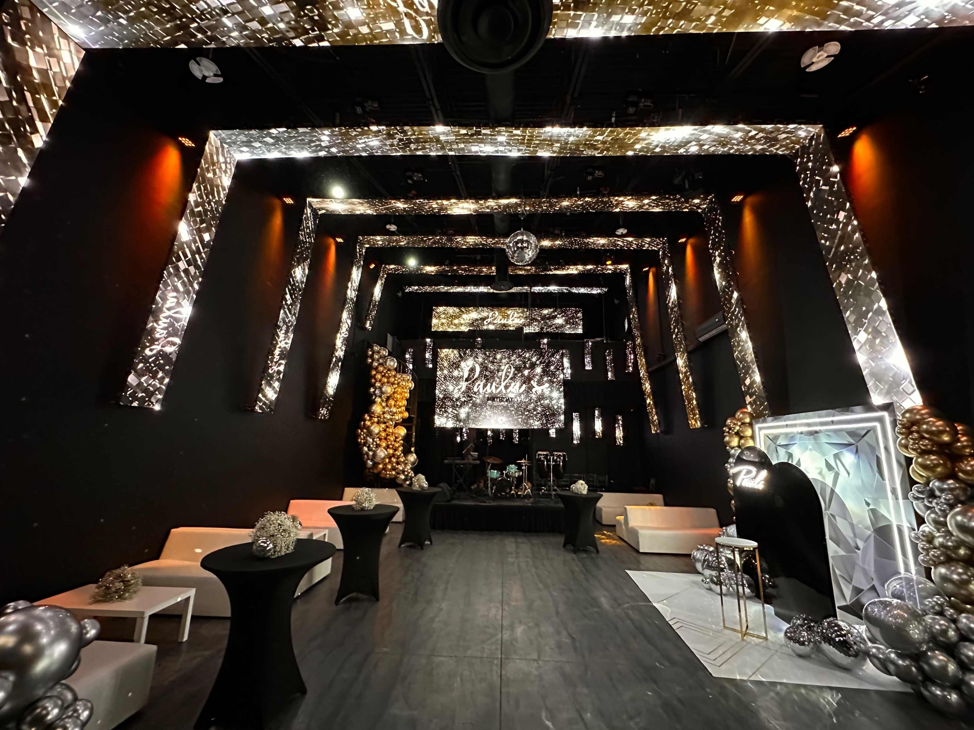 The image shows a decorated event space with shimmering lights, an elevated stage, and seating areas arranged around the edges.