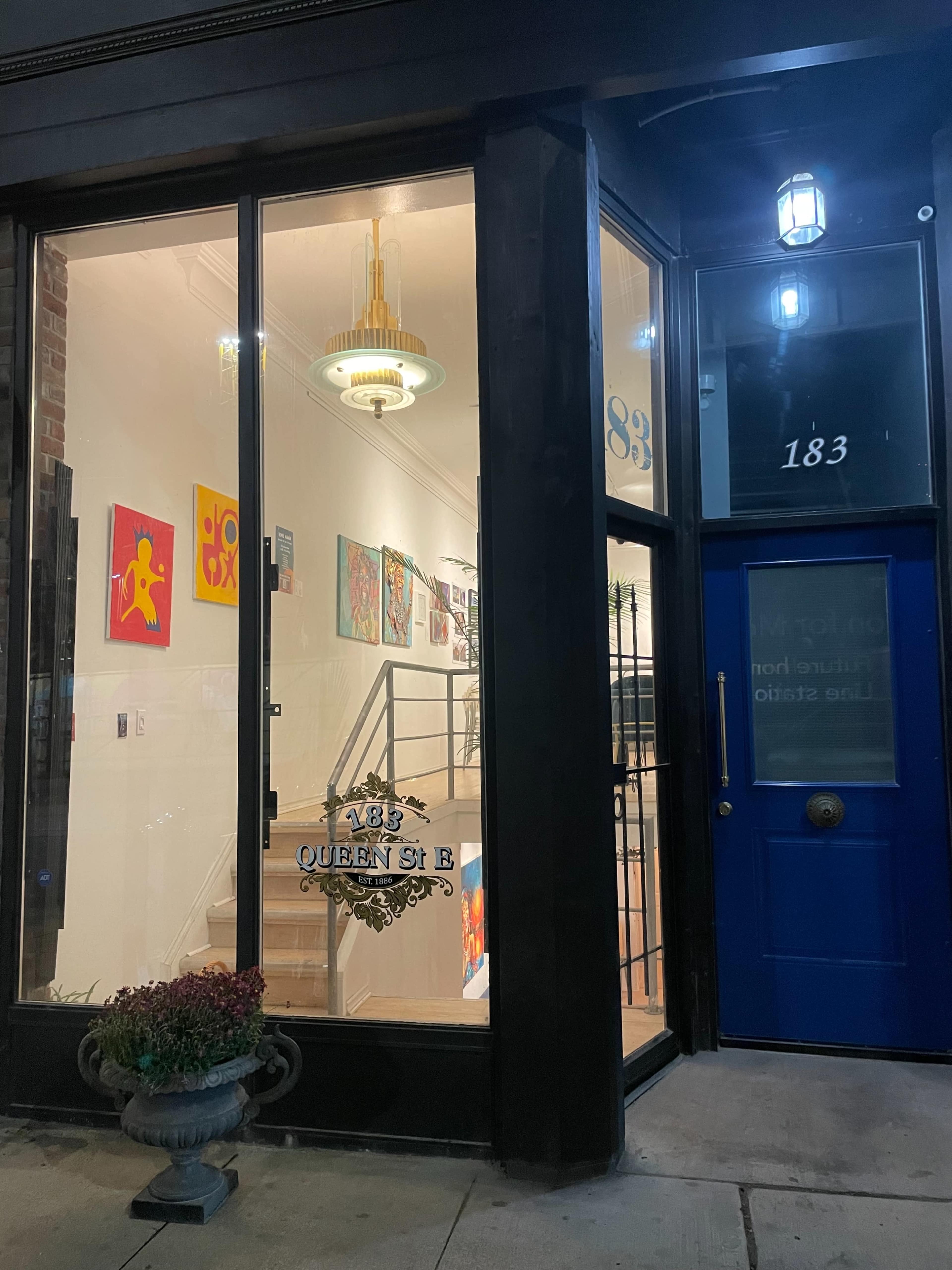 The image shows a storefront with large windows displaying colorful artwork on the walls and a blue door.