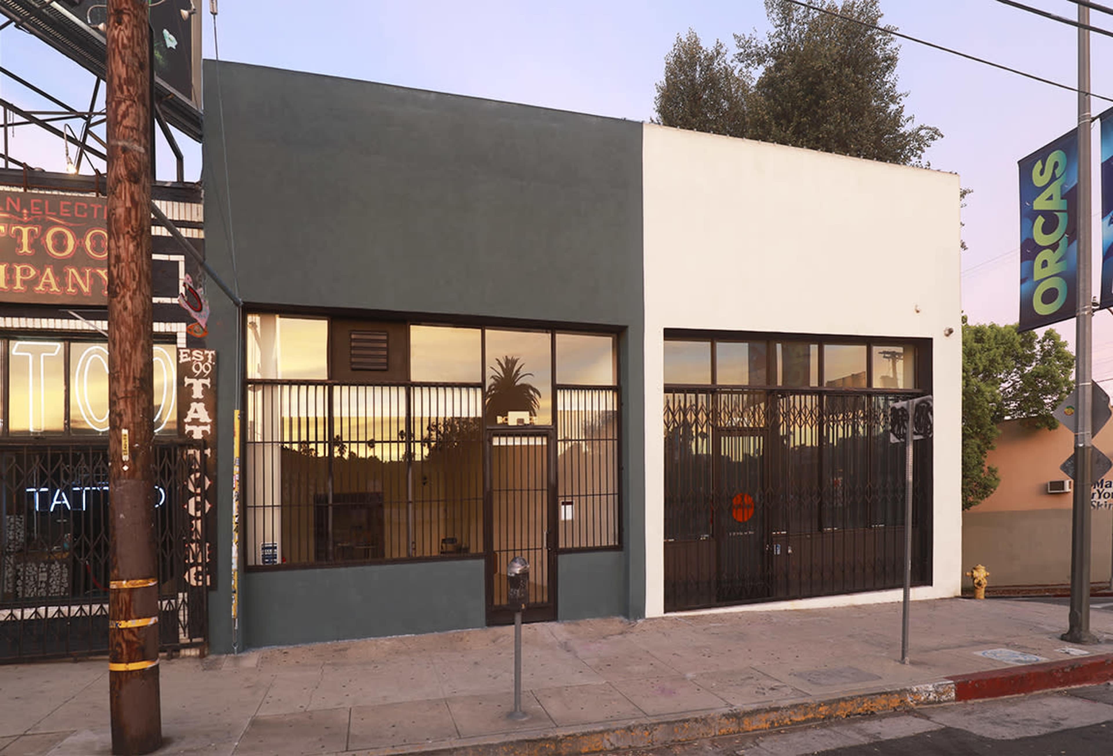 The image shows a modern two-tone building with large windows and a security gate, situated on a city street.