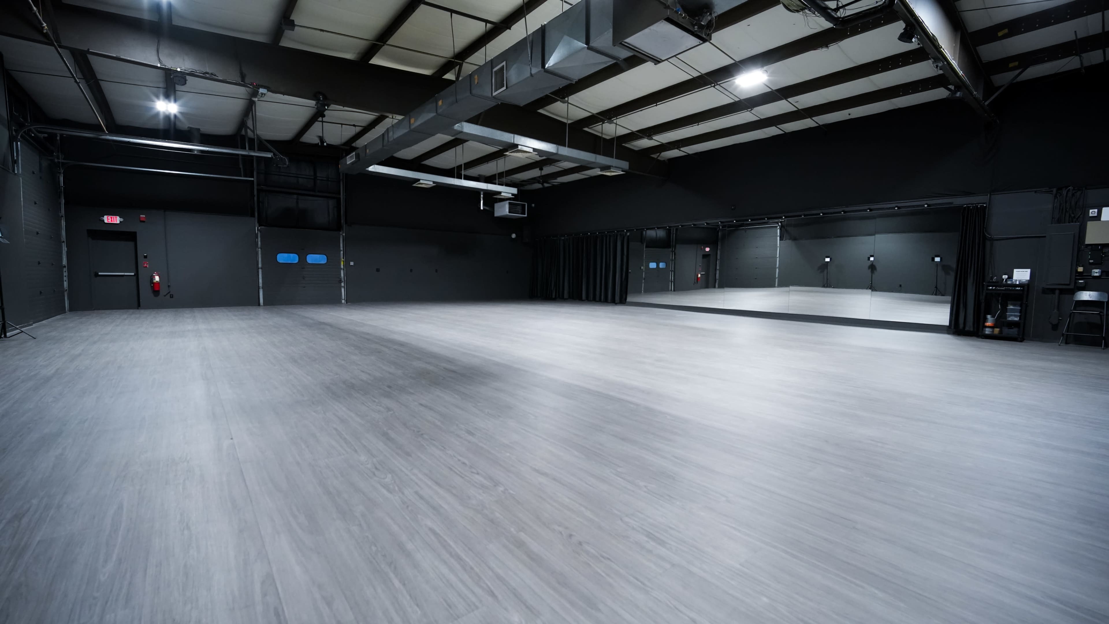 The image shows a large, empty dance studio with smooth gray flooring and mirrors along one wall.