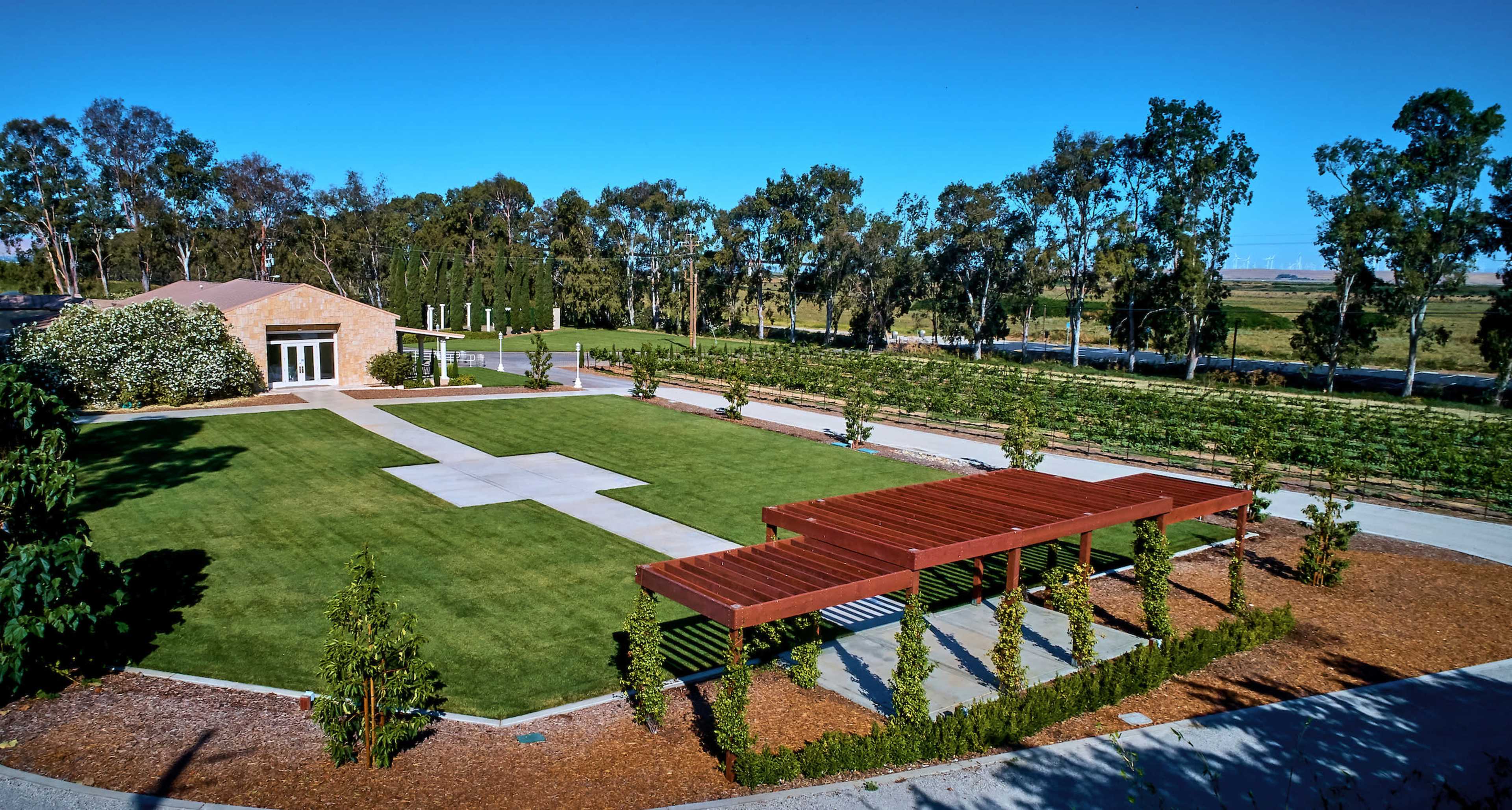 A landscaped outdoor area featuring a manicured lawn, a stone building, and several rows of trees along the perimeter.