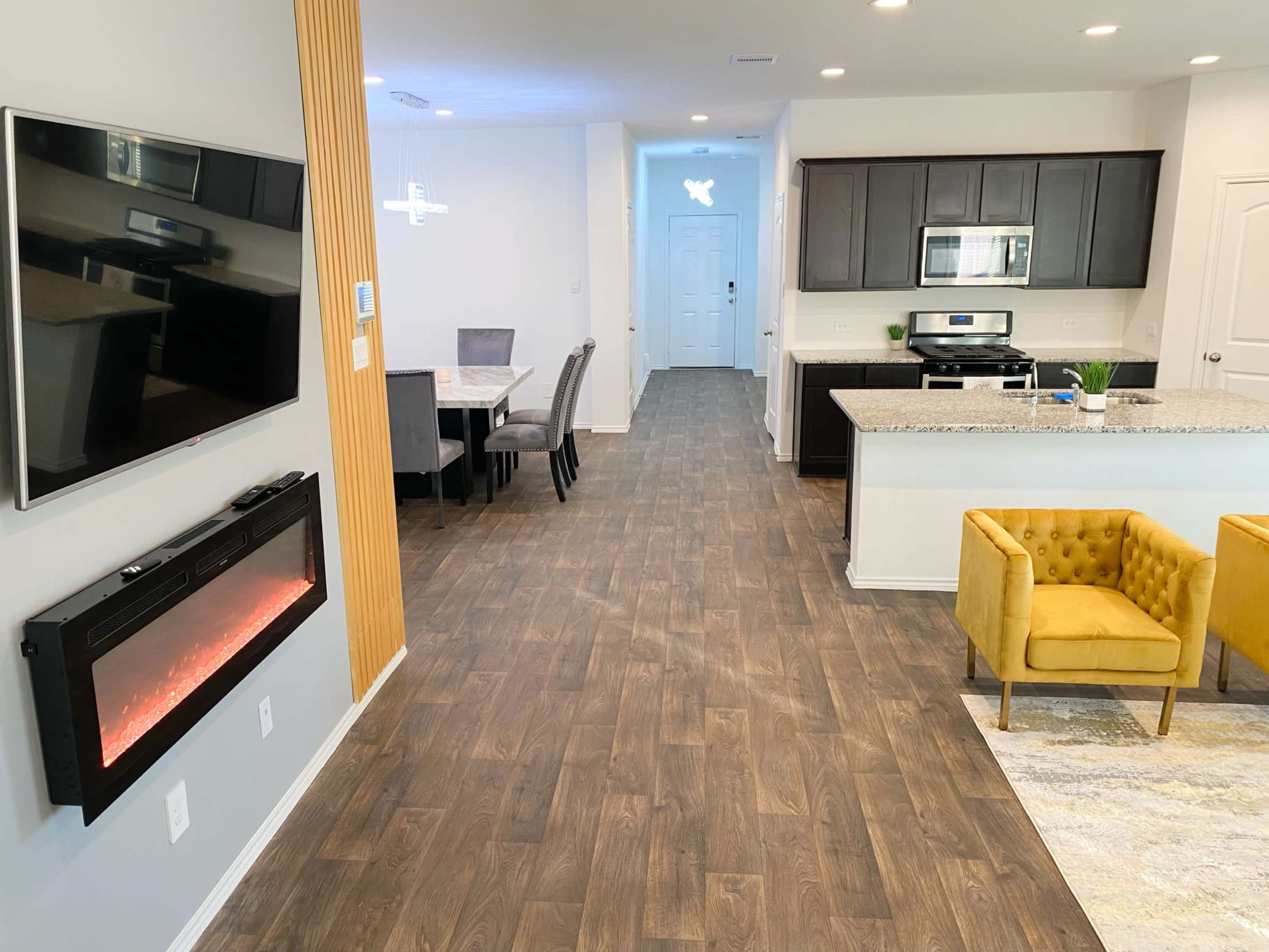 A modern living space featuring a kitchen with dark cabinetry, a dining area with a table and chairs, and a cozy sitting area with a yellow armchair.